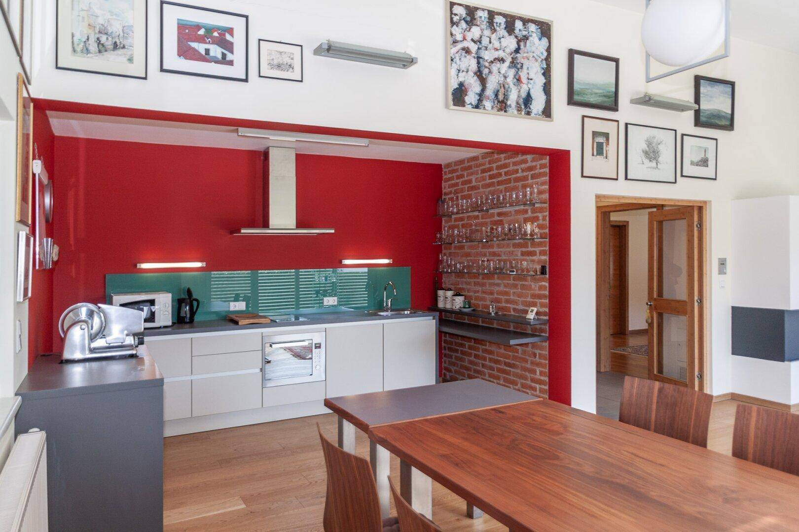 Offene Küche mit roter Wand, Backsteinakzenten und Esstisch, verbunden mit dem Wohnbereich.