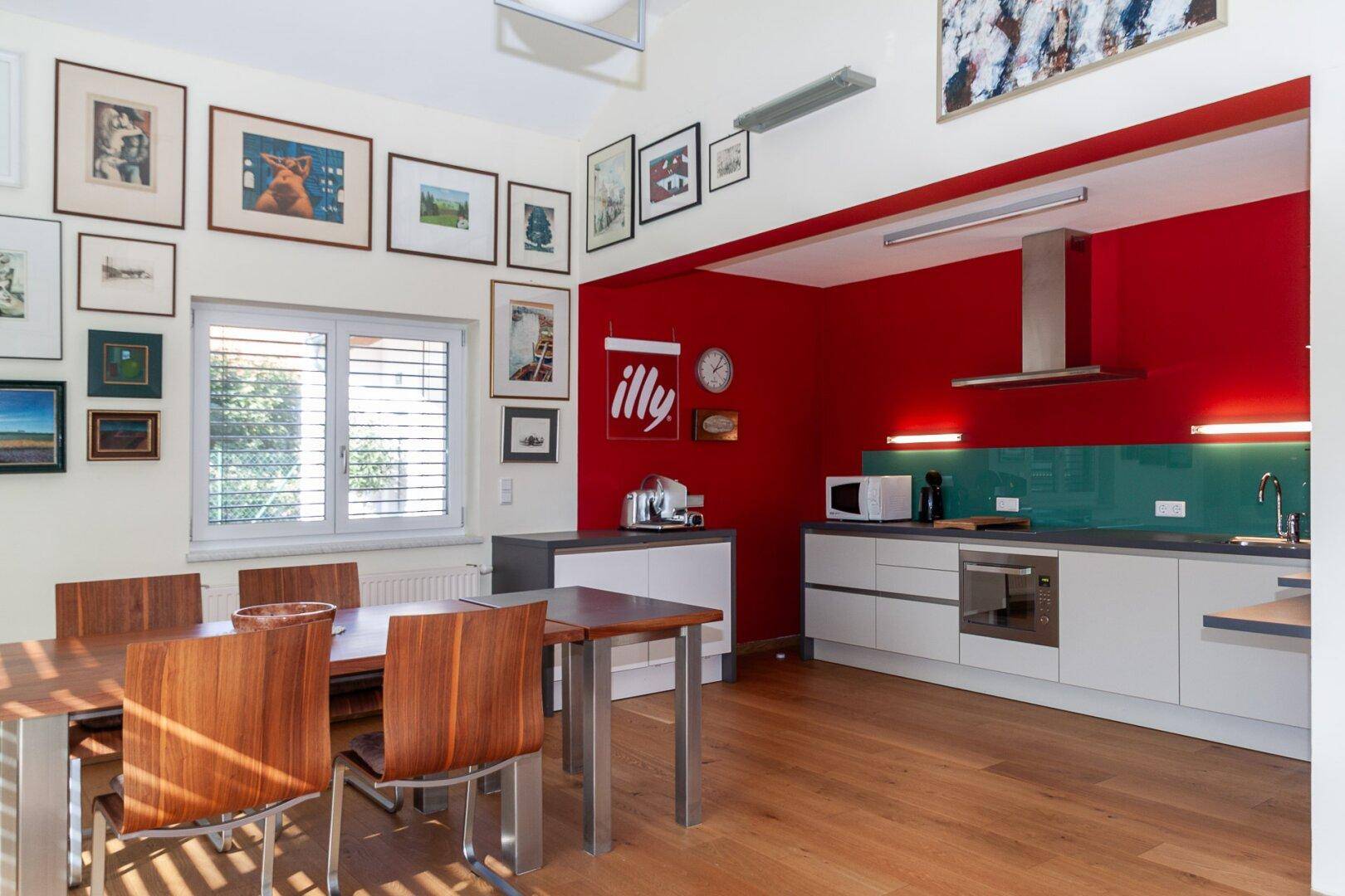Essbereich mit Holztisch und Stühlen, angrenzend an eine moderne Küche mit roter Akzentwand.
