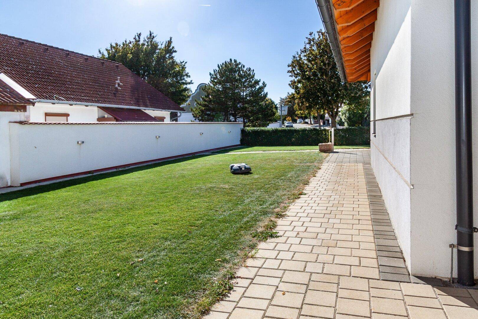 Gepflegter Rasenbereich neben dem Haus mit gepflastertem Weg und einer niedrigen Mauer.