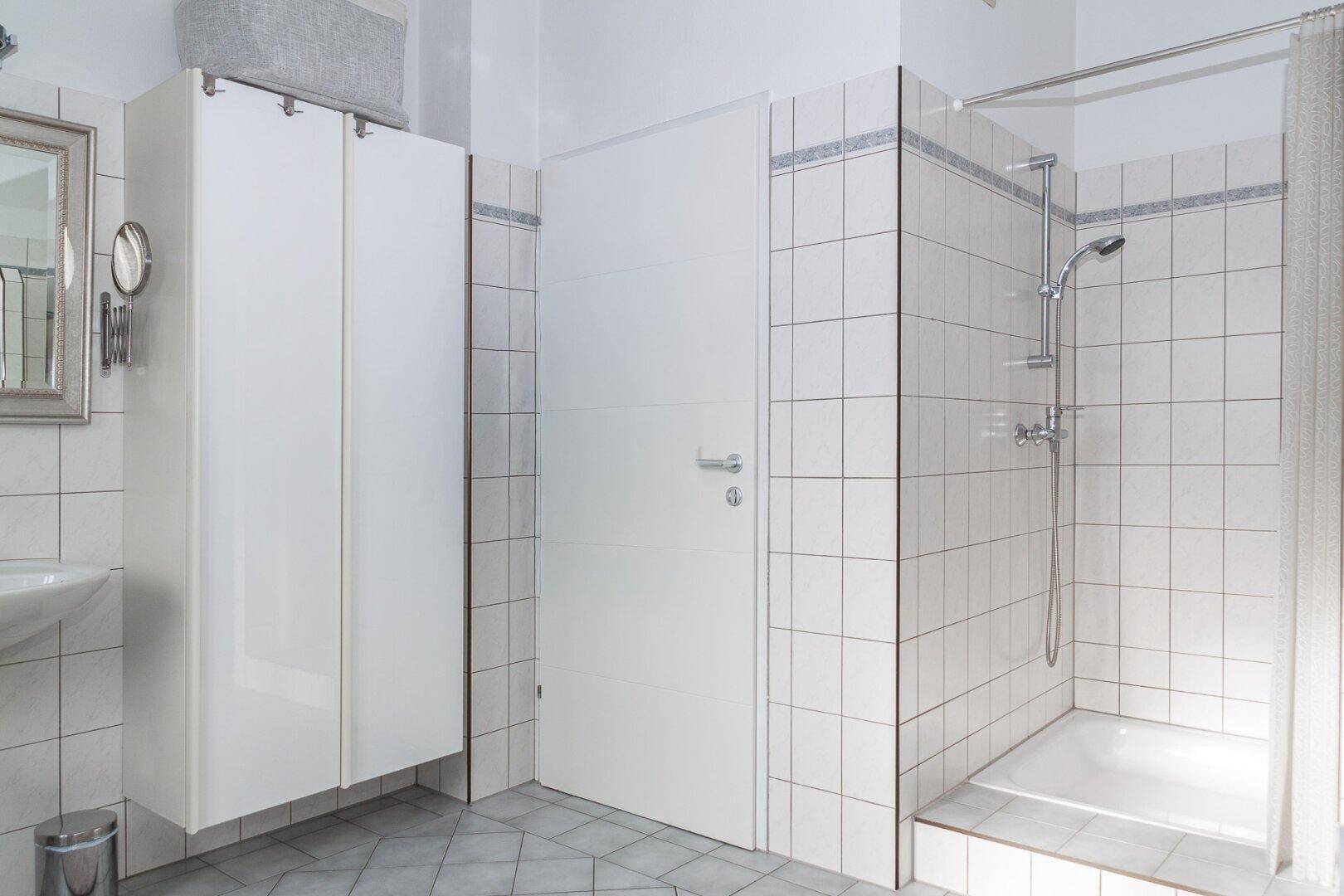 Badezimmer mit Duschbereich, weißen Fliesen und praktischem Spiegelschrank.