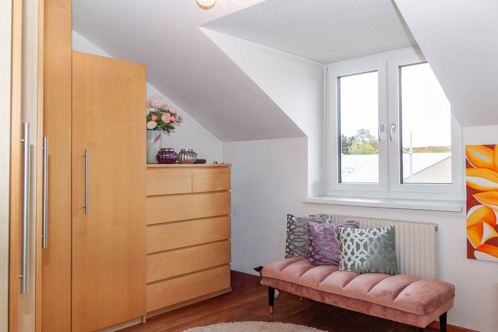 Schlafzimmer im Dachgeschoss mit Holzschrank, Kommode und Dachschräge.