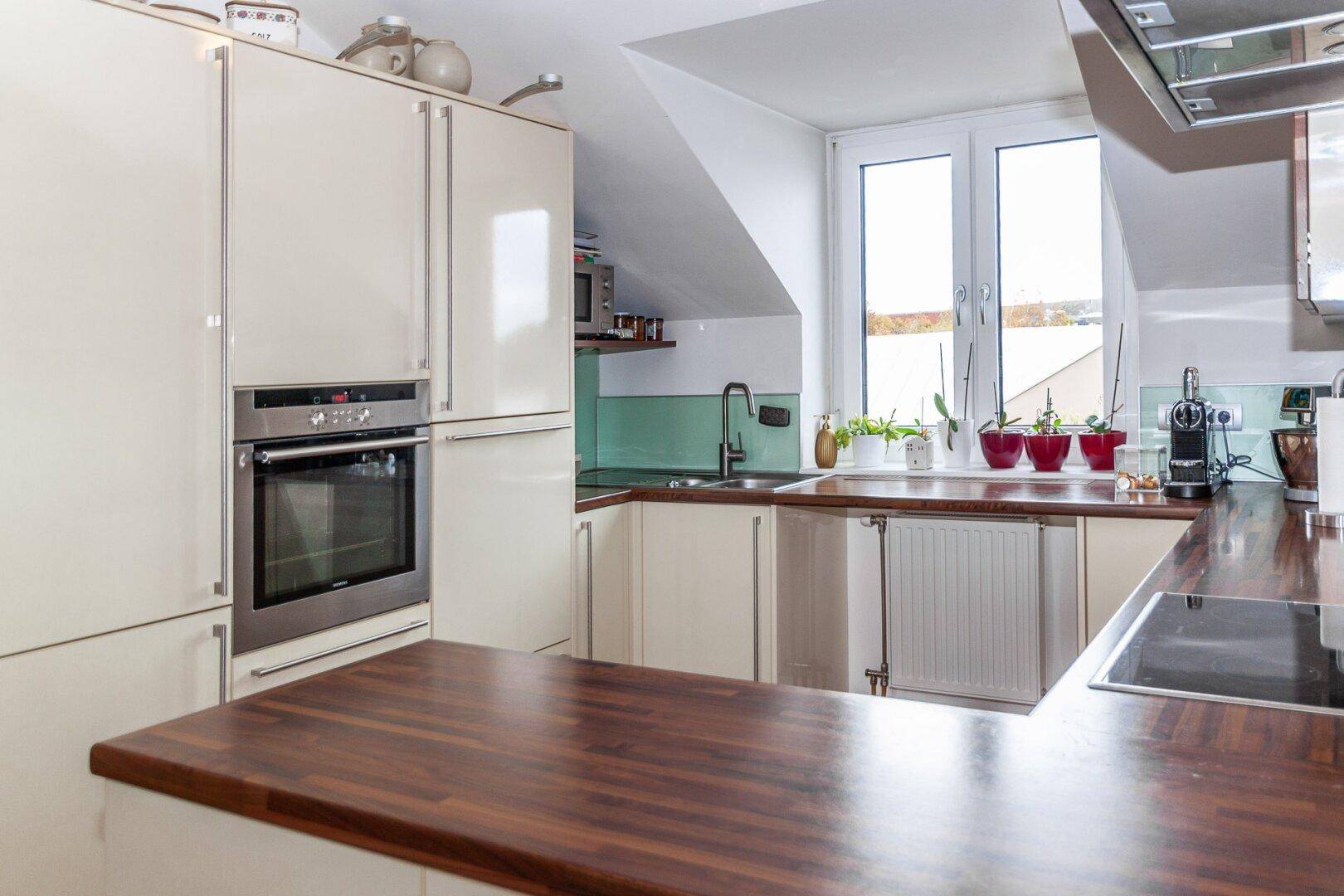 Moderne Küche im Dachgeschoss mit Einbaugeräten, Holz-Arbeitsplatten und Dachschräge.