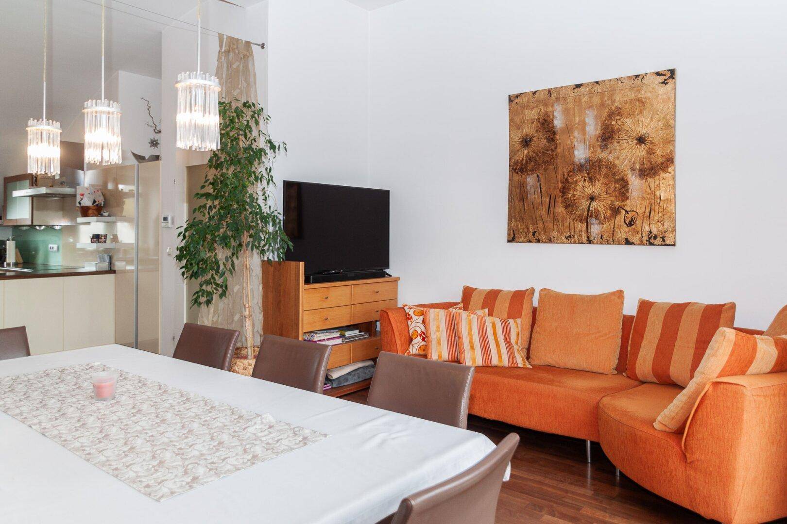 Gemütlicher Wohnbereich mit orangefarbenem Sofa, Kunstwerk und Blick auf den Essbereich.