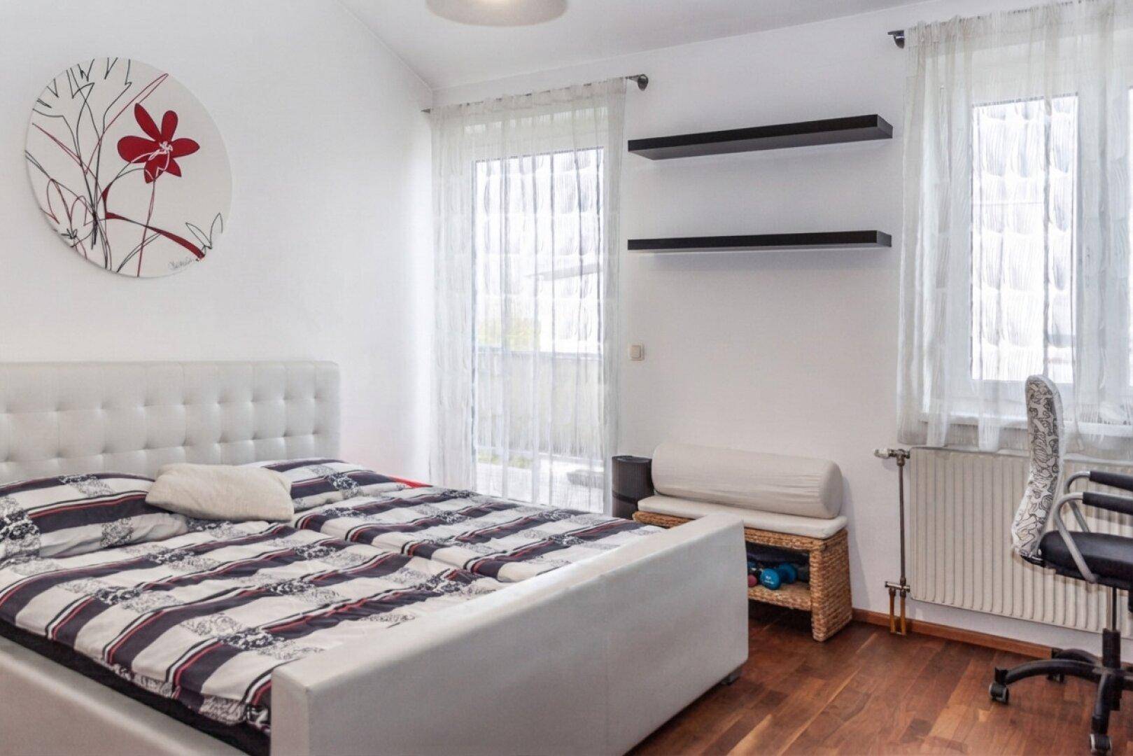 Helles Schlafzimmer mit Doppelbett, Holzfußboden und Zugang zu einem Balkon.
