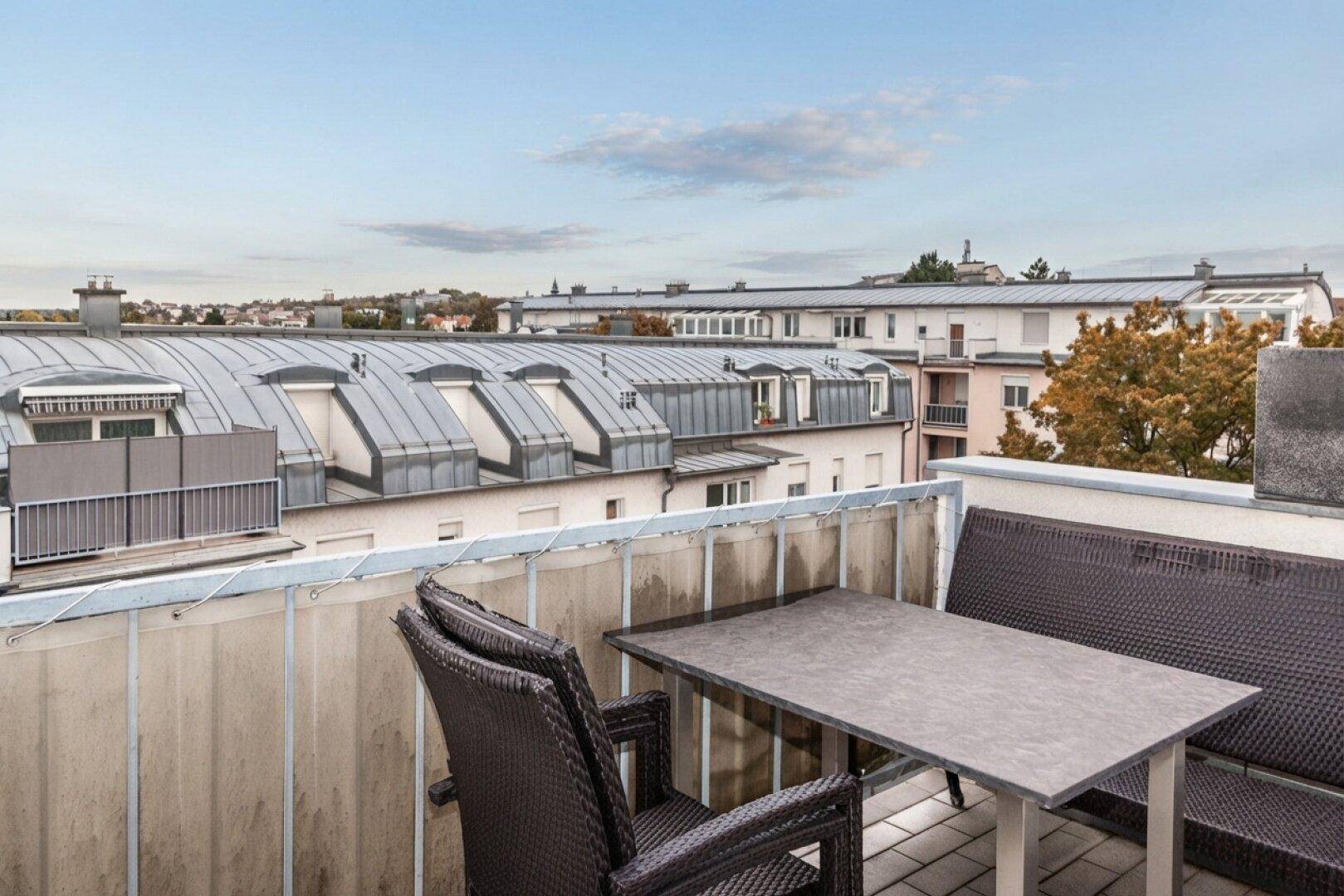 Möblierter Balkon mit Tisch und Stühlen, bietet eine weite Aussicht über die Dächer.