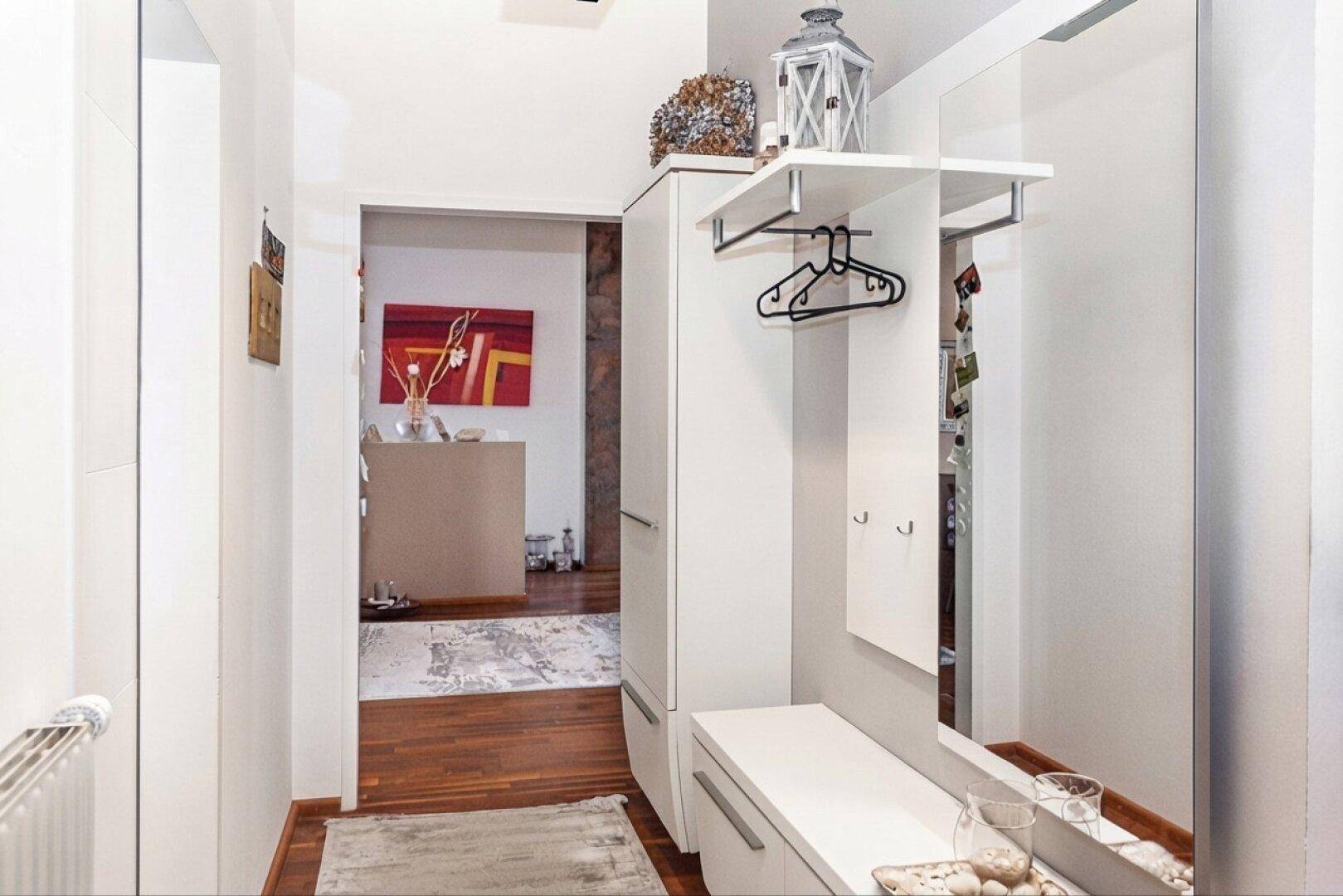 Heller Flur mit Garderobe, Spiegel und Holzfußboden, der zu weiteren Räumen führt.