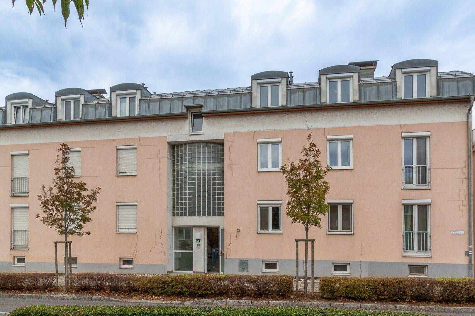 Mehrfamilienhaus mit rosafarbener Fassade, vielen Fenstern und französischen Balkonen.