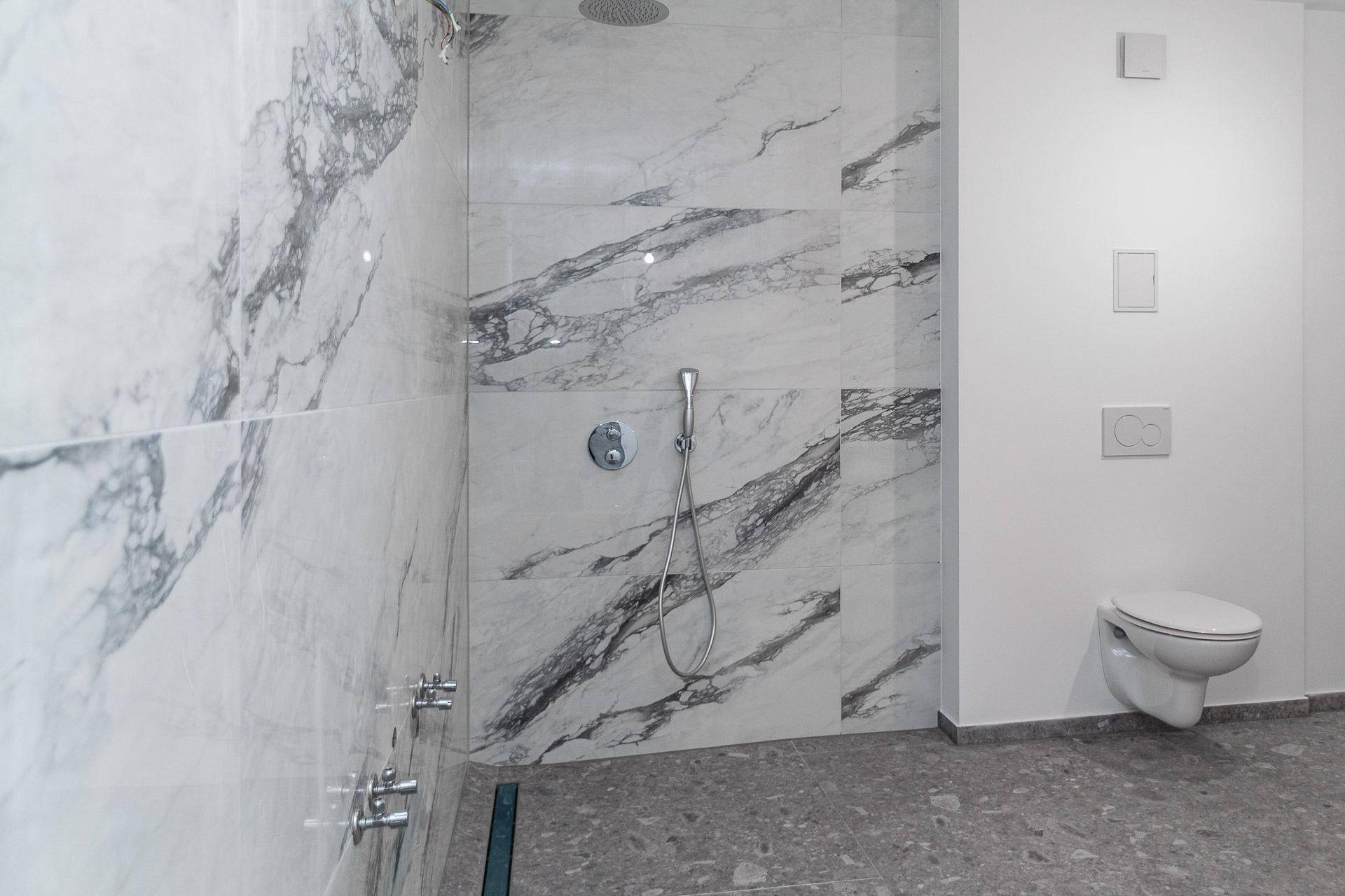 Geräumiges Badezimmer mit moderner Regendusche, Handbrause und Wand-WC.