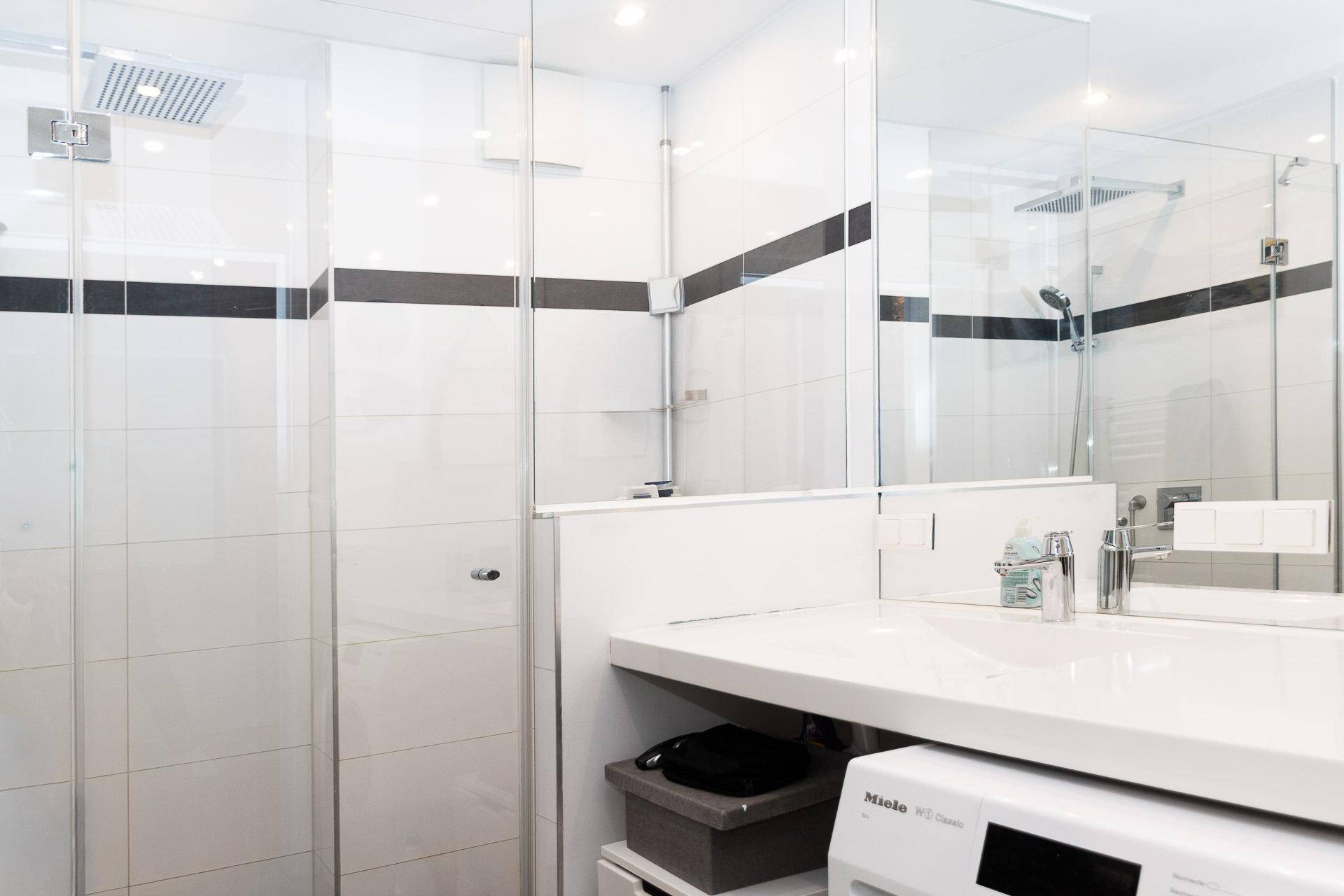 Modernes Badezimmer mit großer begehbarer Dusche, Waschbecken und integrierter Waschmaschine.