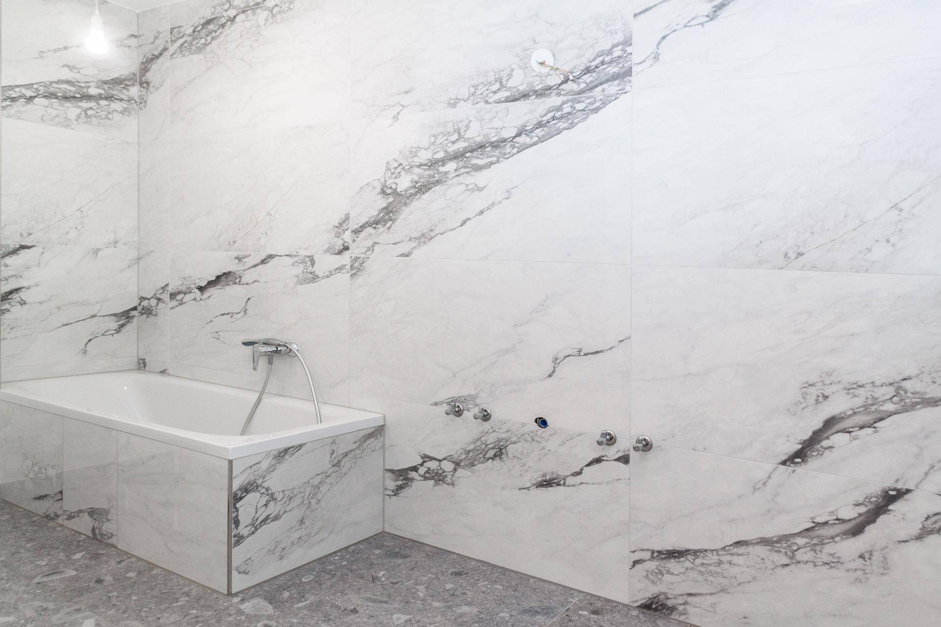 Elegantes Badezimmer mit Badewanne und großformatigen Marmorfliesen an den Wänden.