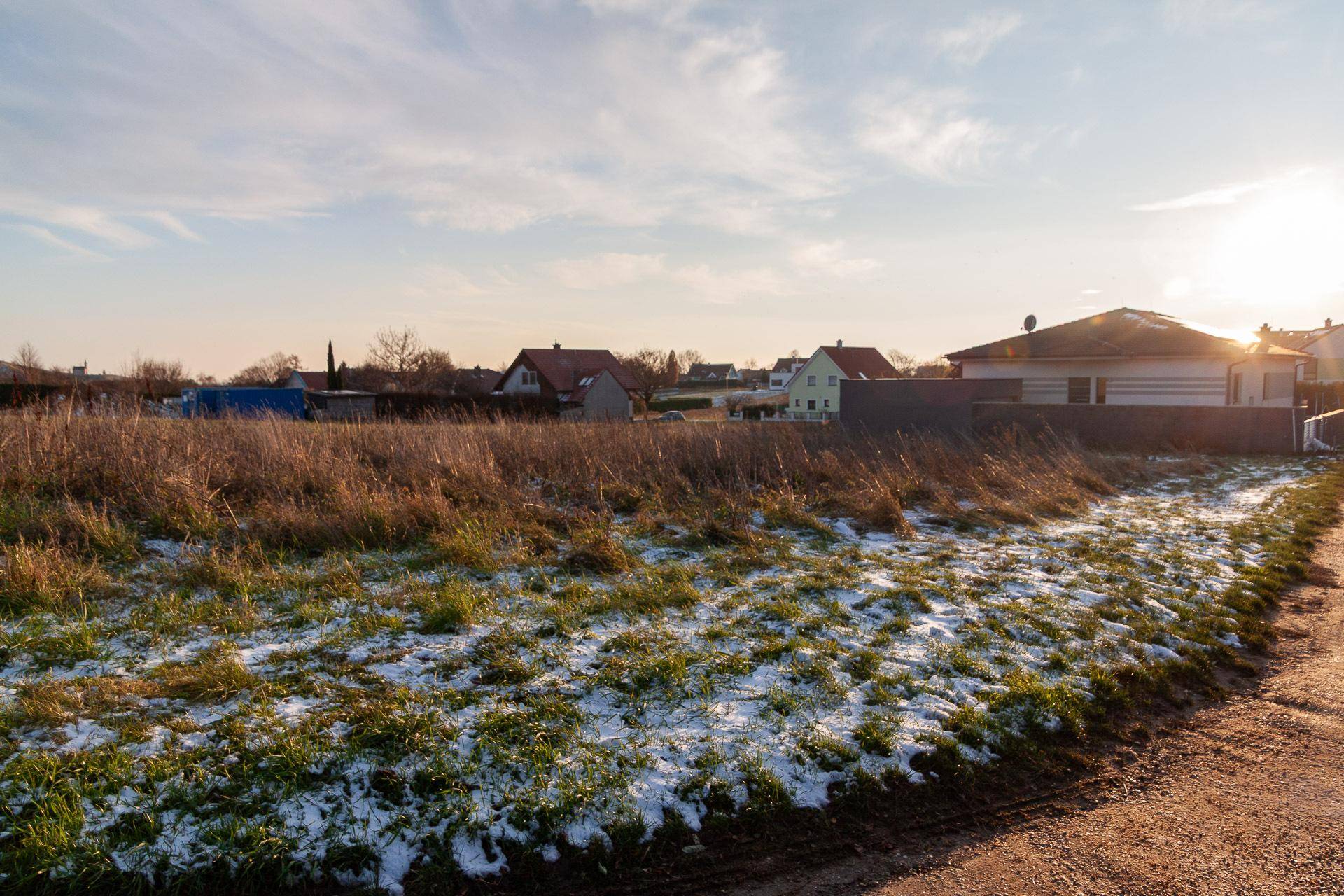 Blick über ein schneebedecktes Feld auf eine Siedlung mit Wohnhäusern unter einem weiten Himmel.