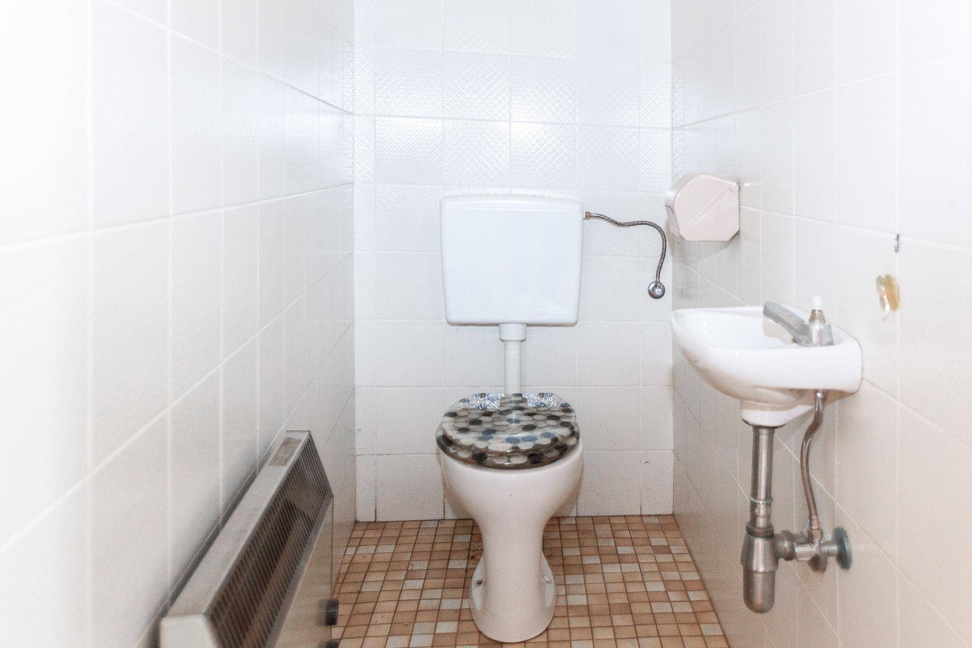 Kleines WC mit Fliesenboden, Toilette und Waschbecken, in einfachem Zustand.