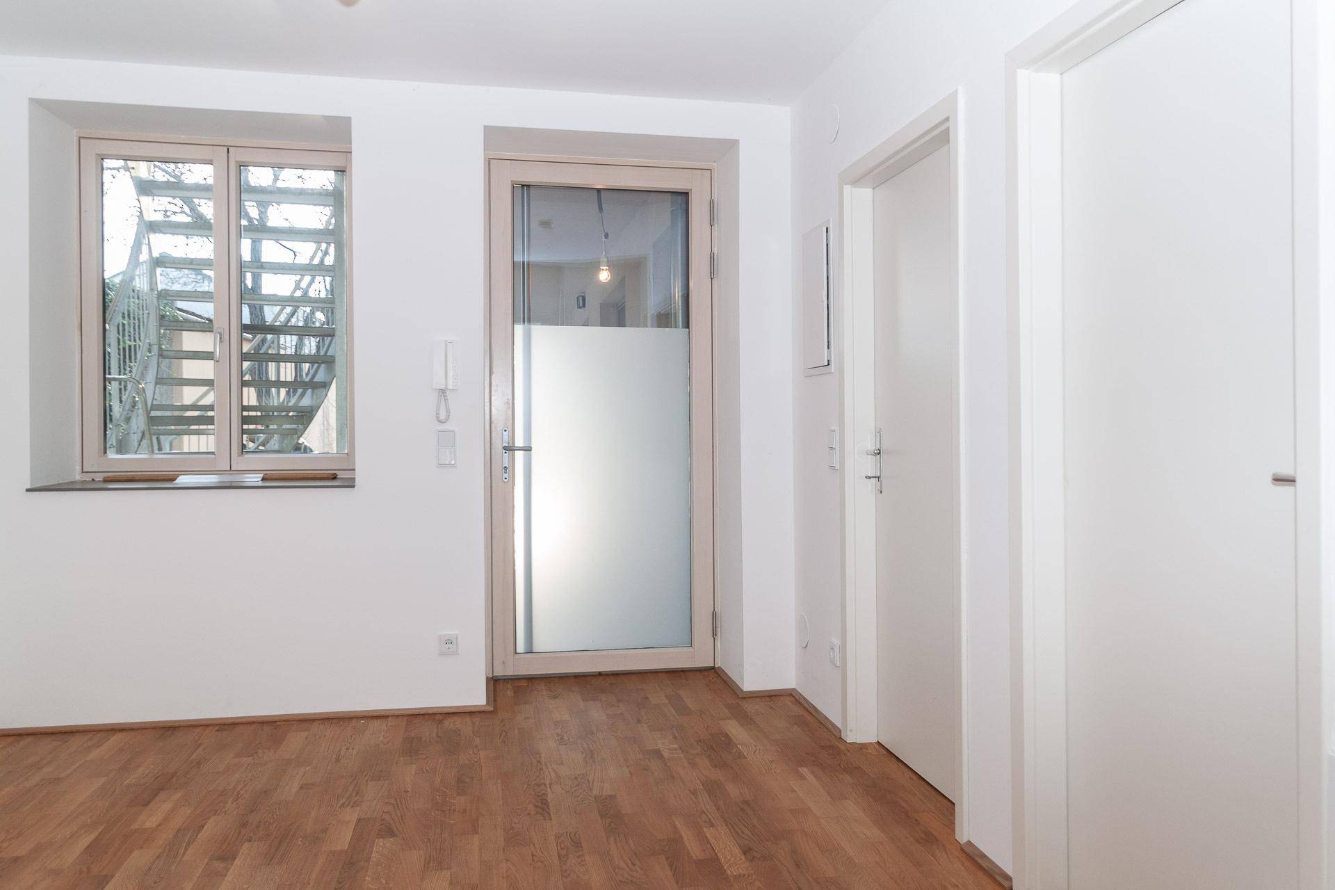 Heller Innenraum mit Holzboden, weiß gestrichenen Wänden und einer Zugangstür.