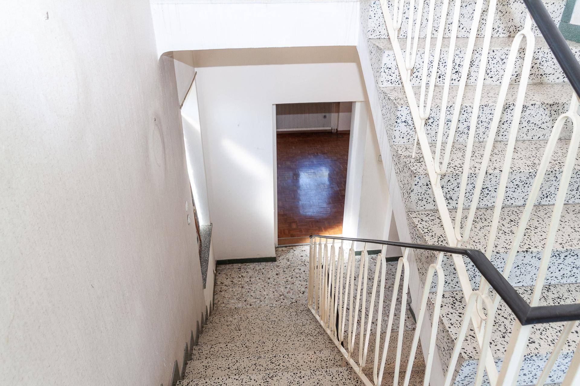 Treppenhaus mit Terrazzostufen und Geländer, das die oberen Etagen erschließt.