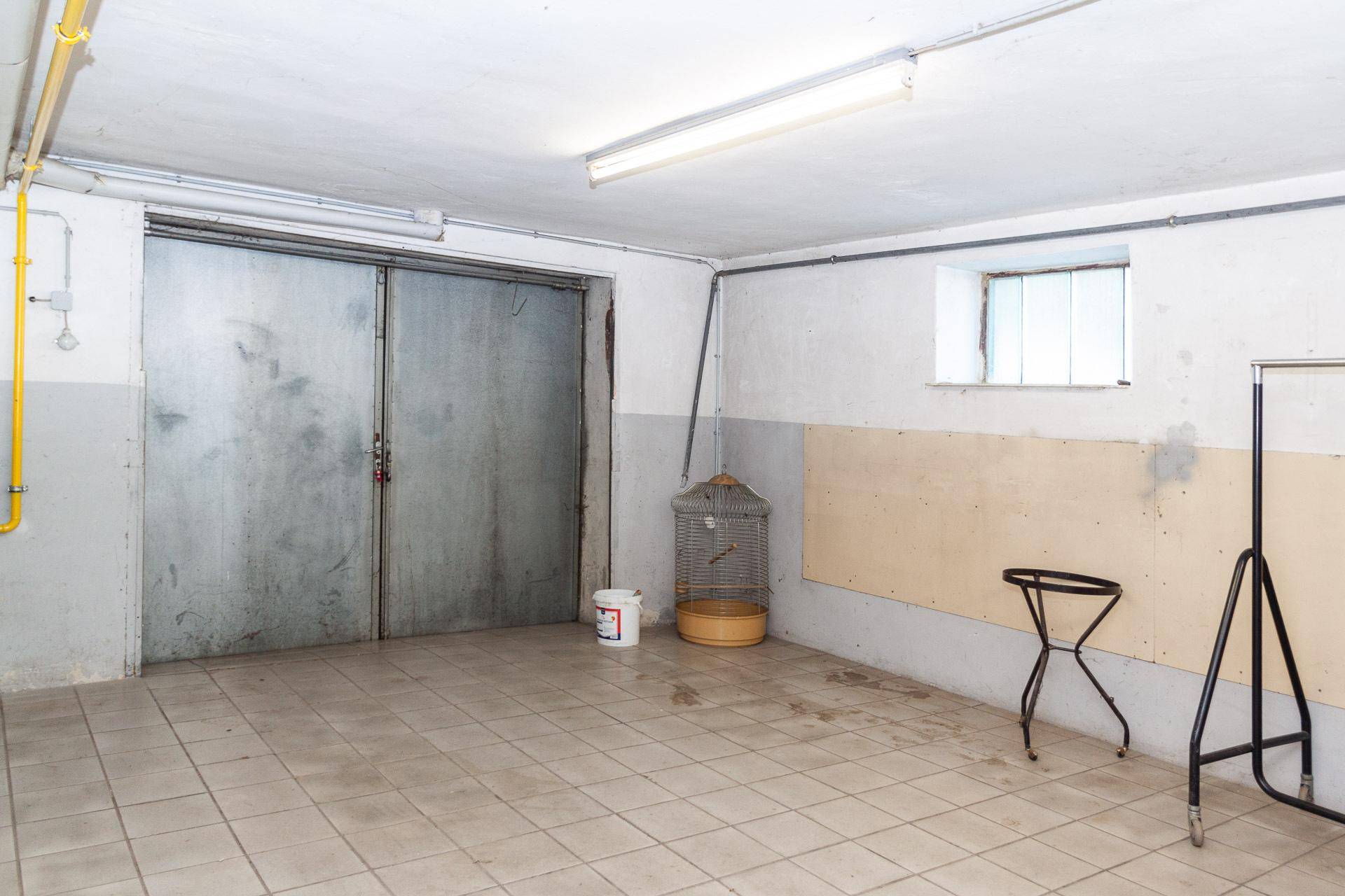 Geräumiger Kellerraum mit Fliesenboden und großen Metalltüren, nutzbar als Garage oder Lager.