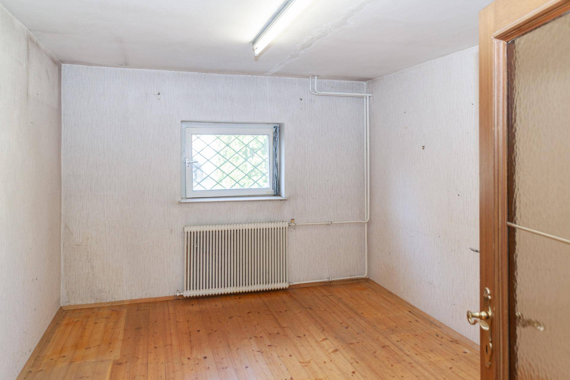 Einfacher Kellerraum mit Holzfußboden und Fenster, geeignet für Lagerzwecke.