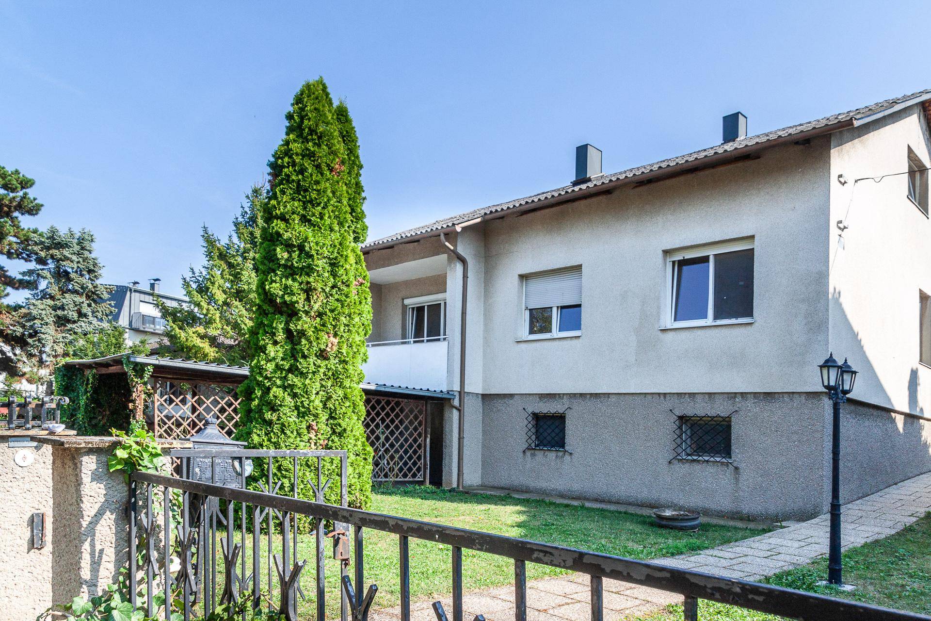 Seitenansicht des Hauses mit Gartenbereich, hohen Bäumen und einem gepflasterten Weg.