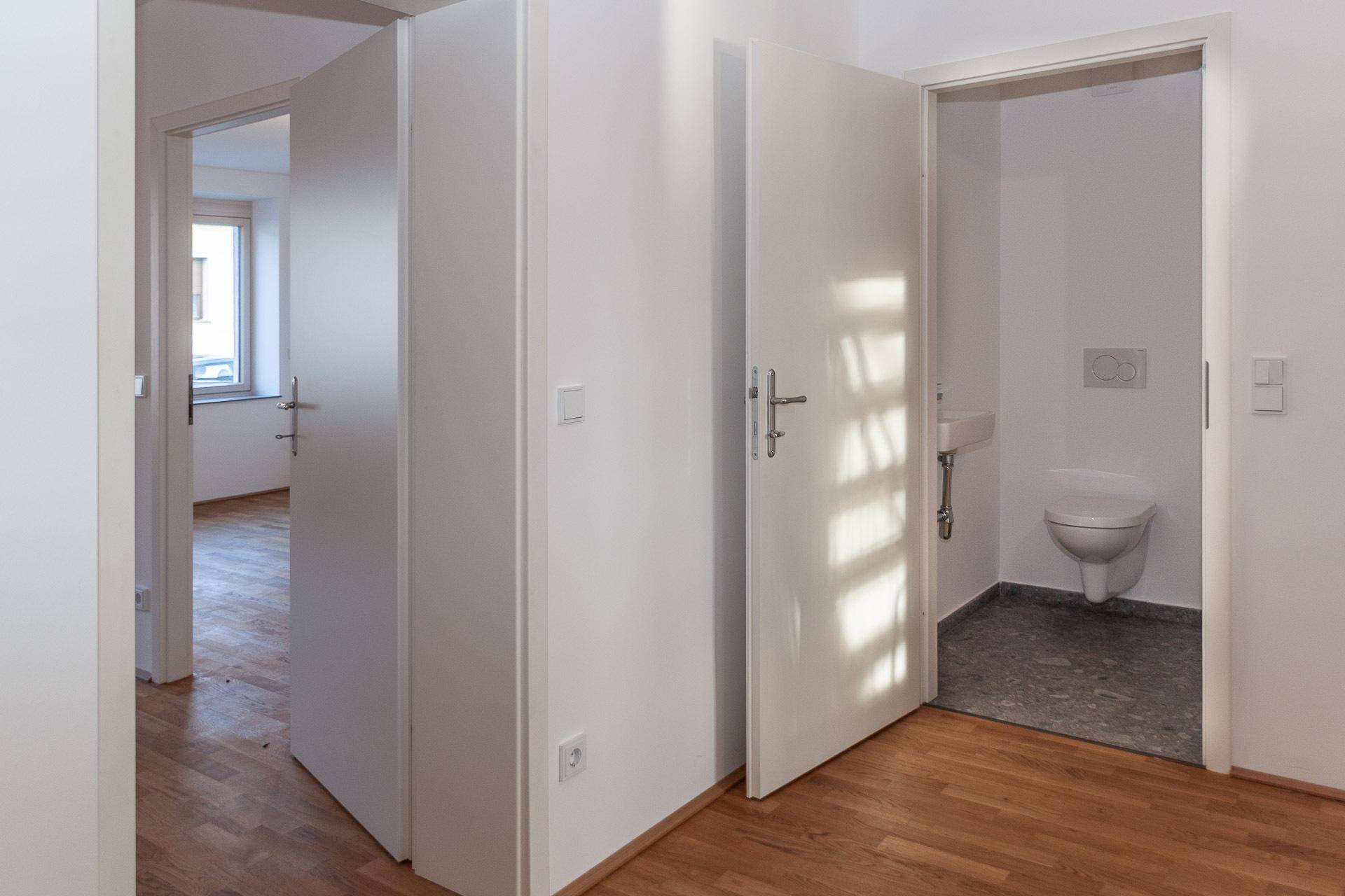 Heller Flur mit Holzboden und Blick in ein modernes Badezimmer mit Toilette.