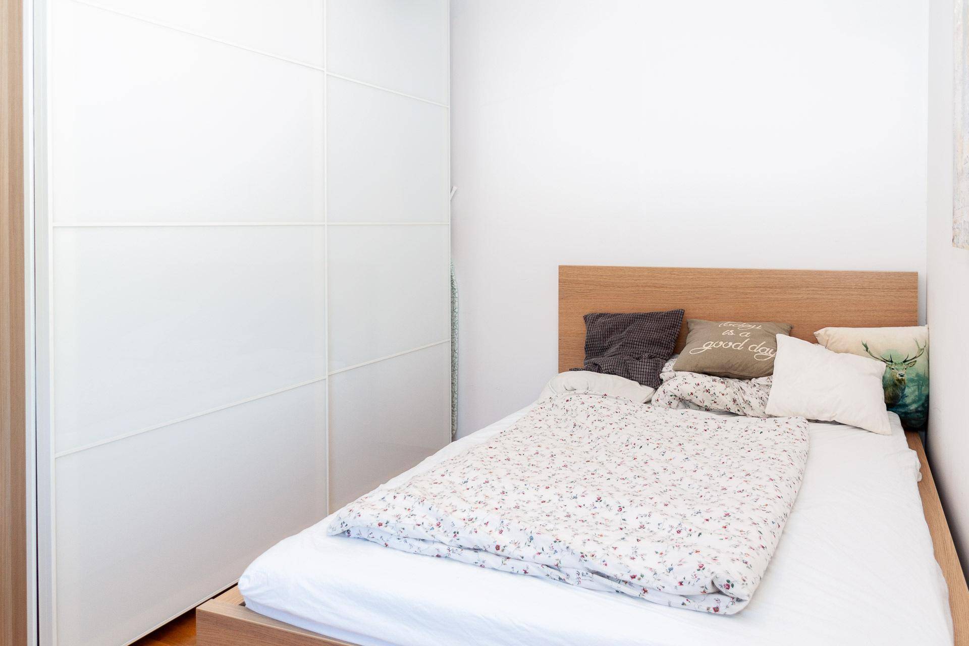 Schlafzimmer mit Holzbett, weißem Schrank und schlichter, heller Einrichtung.