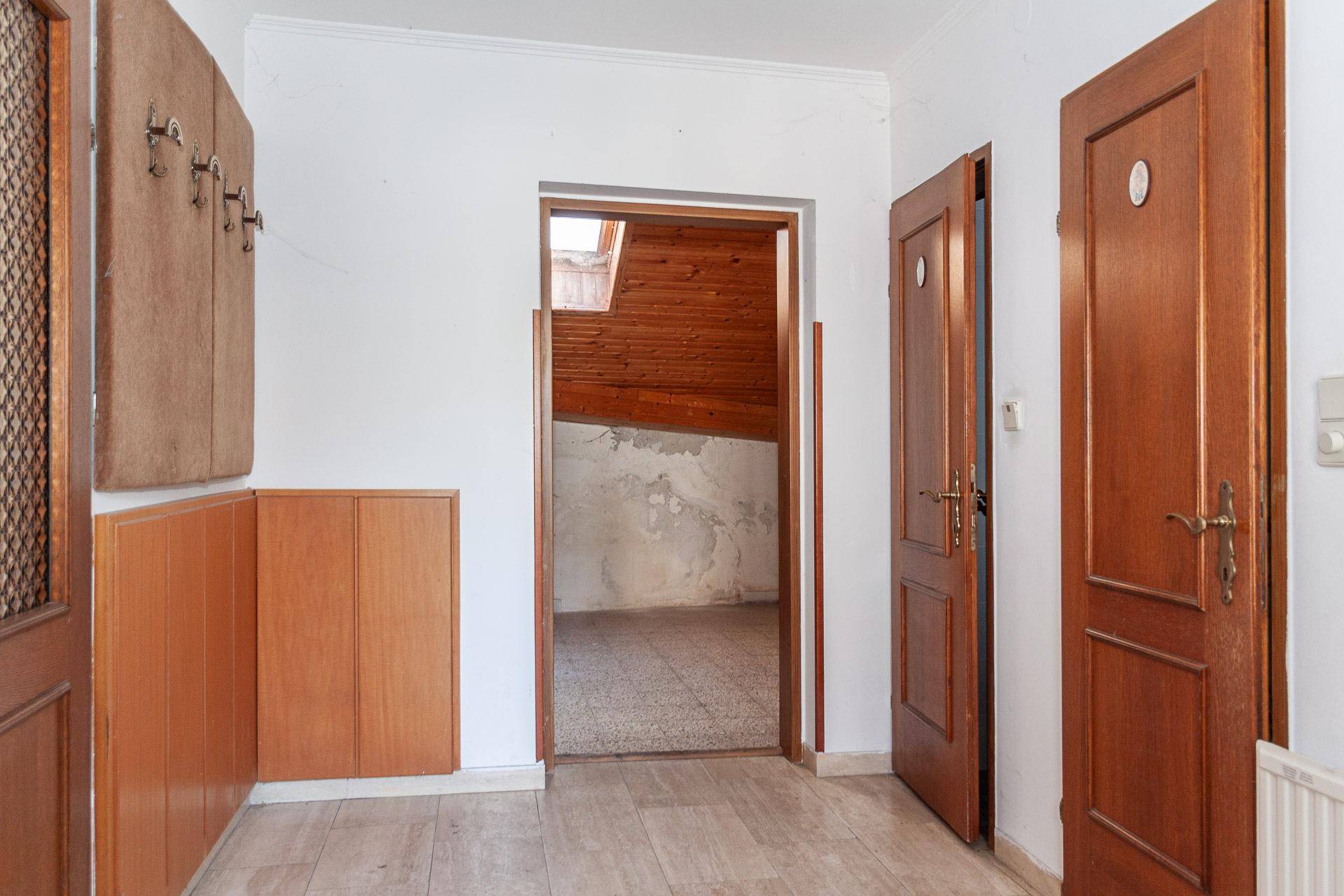 Flur mit Holzschränken und Zugang zu einem Dachzimmer mit Holzverkleidung.