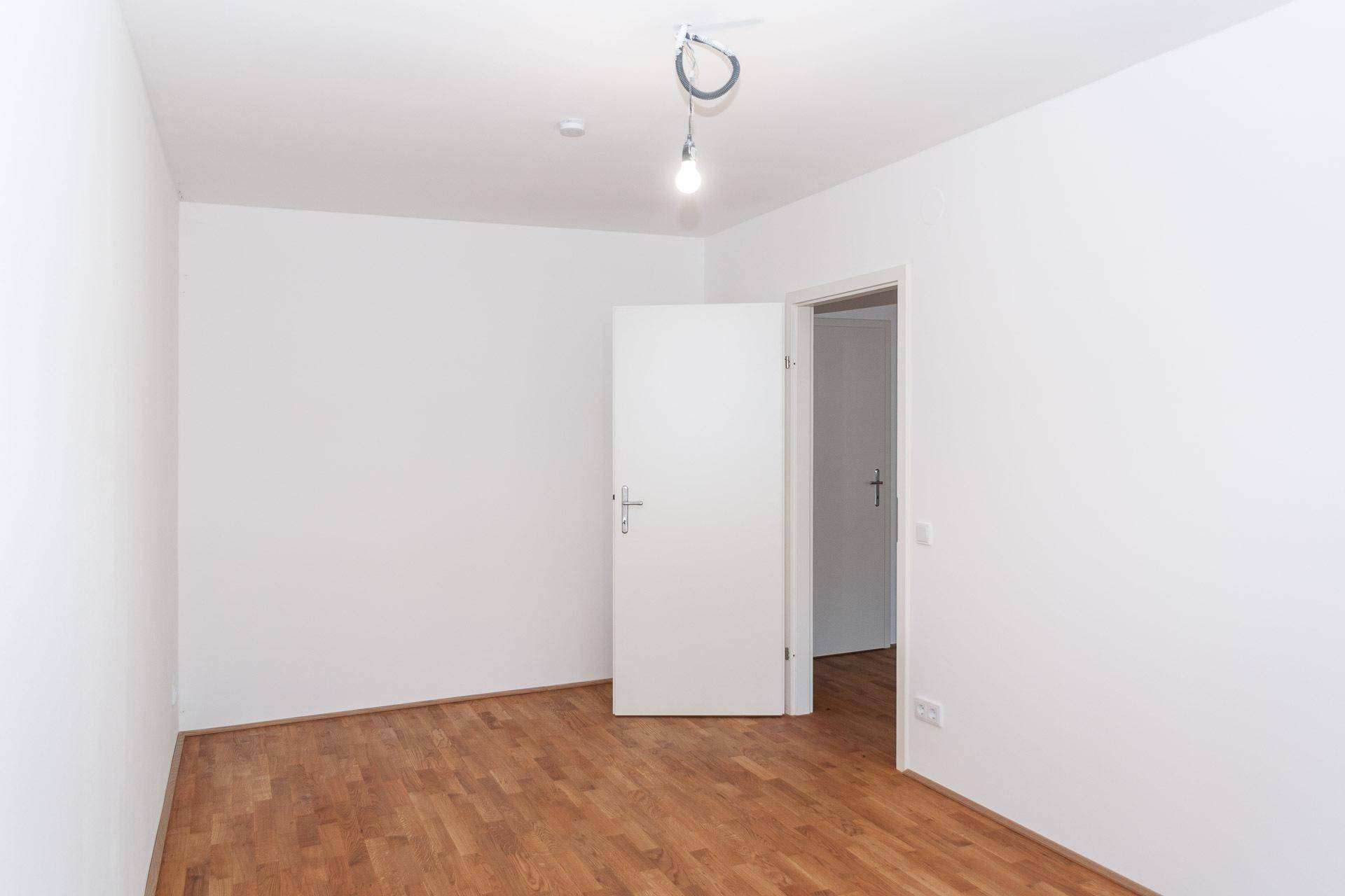 Helles Schlafzimmer mit Holzboden und weiß gestrichenen Wänden, bereit zum Einrichten.