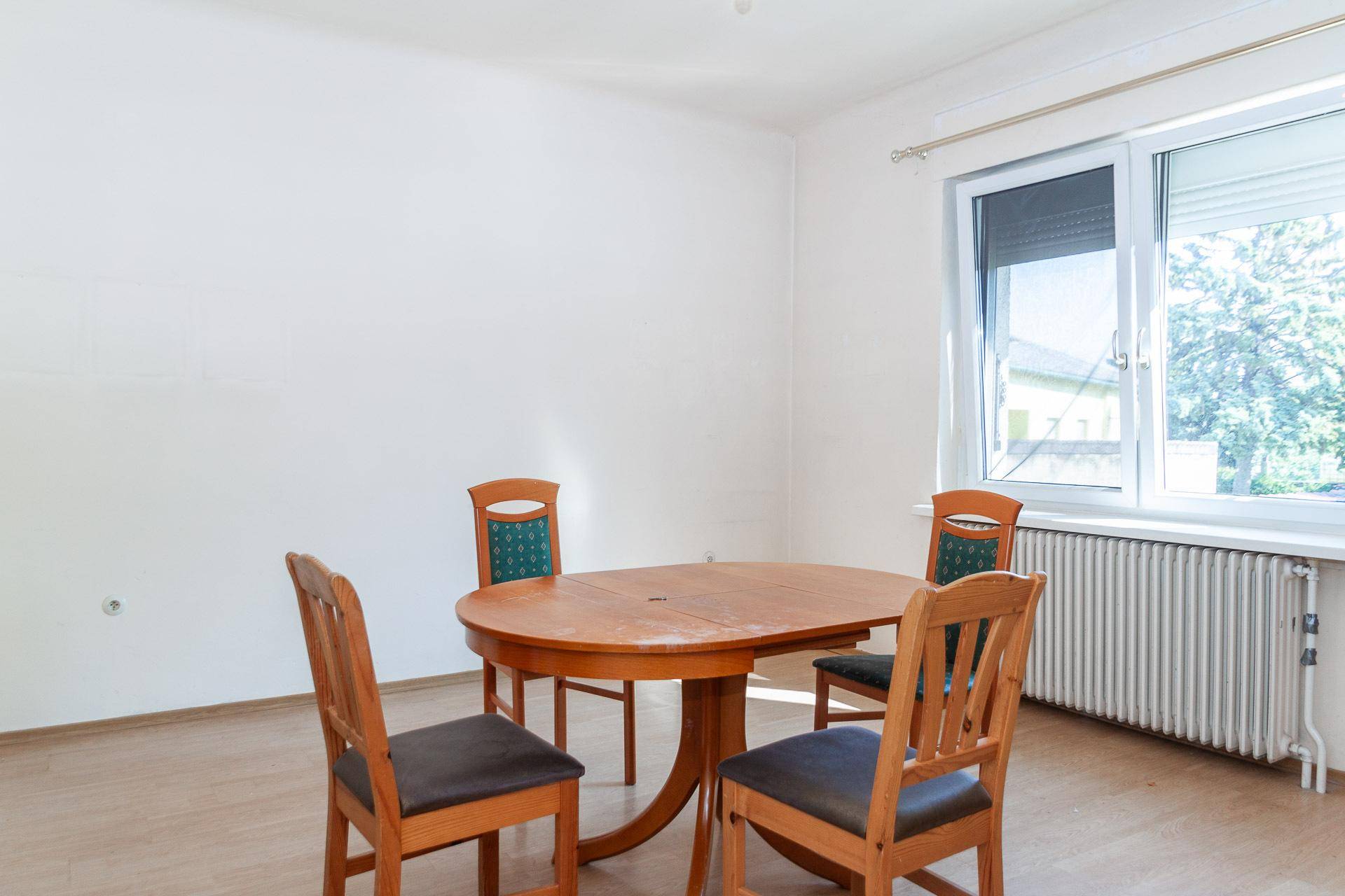 Esszimmer mit Holztisch und Stühlen, großem Fenster und Heizkörper.