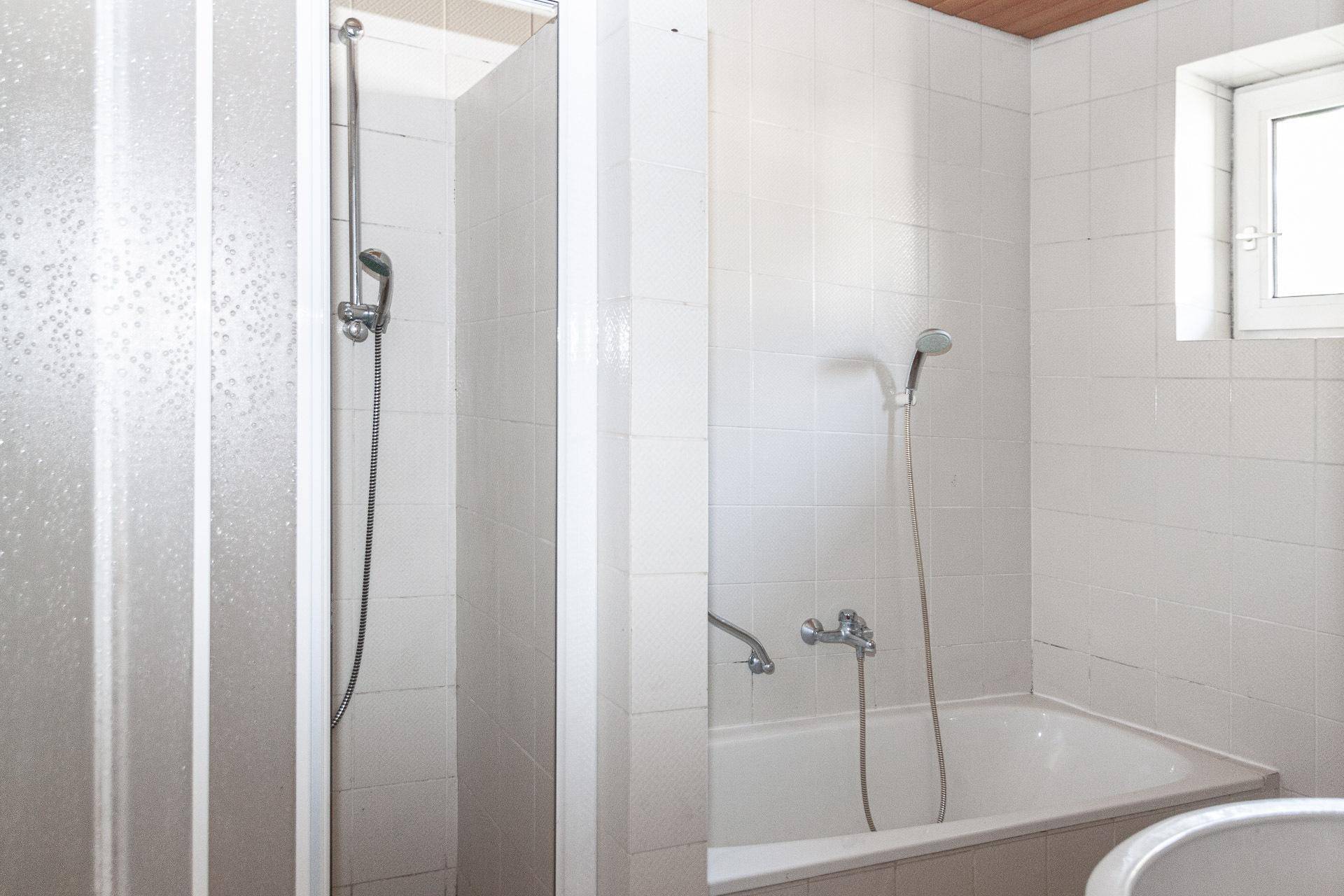 Badezimmer mit Badewanne und Duschbereich, komplett gefliest und mit Fenster.