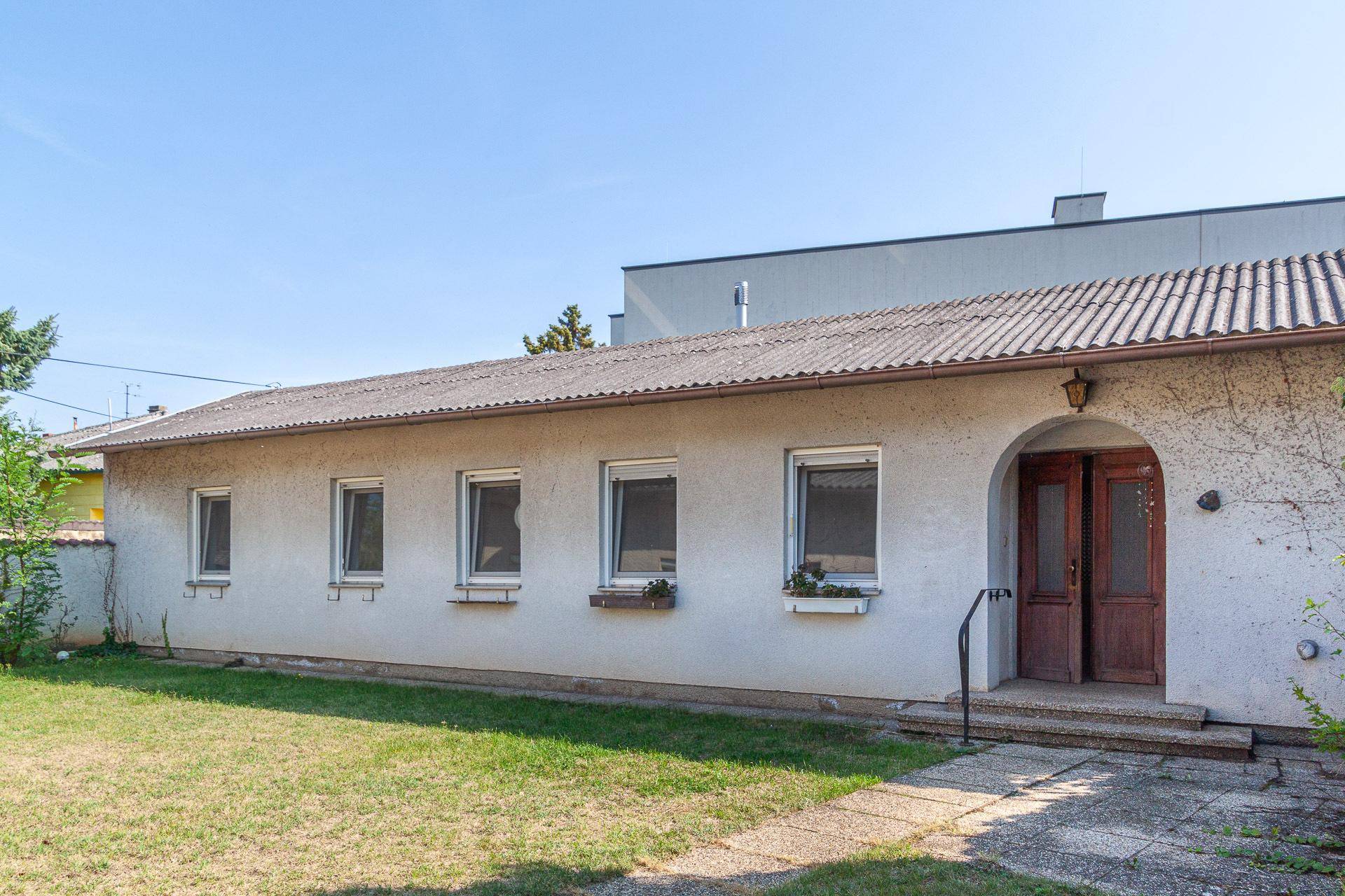 Lange Seitenansicht des Hauses mit mehreren Fenstern und einem gepflegten Garten.