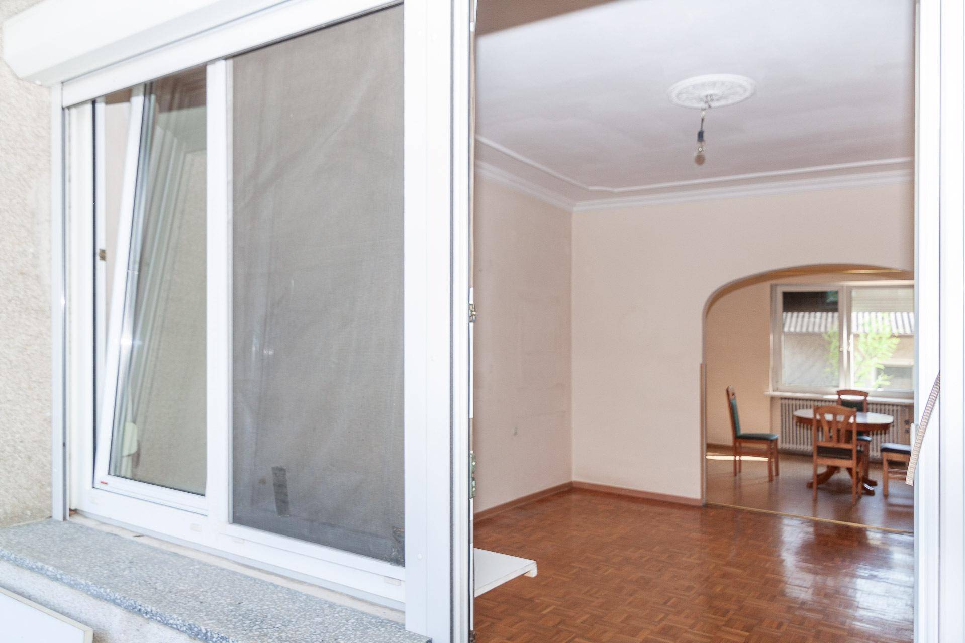 Wohnzimmer mit Parkettboden und direktem Zugang zum Balkon, der viel Licht hereinlässt.