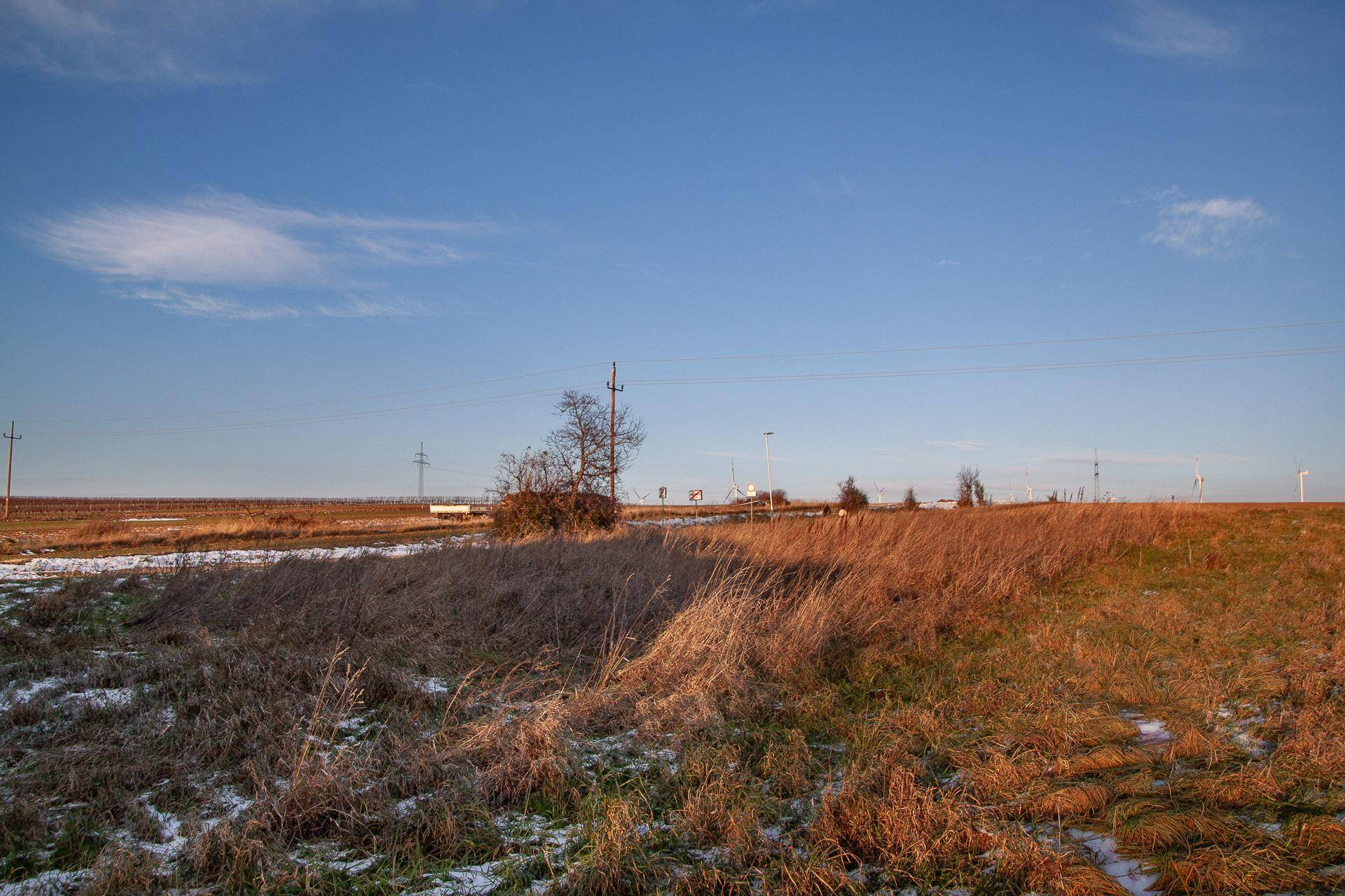 Weitläufige, offene Landschaft mit trockenen Feldern und vereinzelten Schneeflecken unter blauem Himmel.