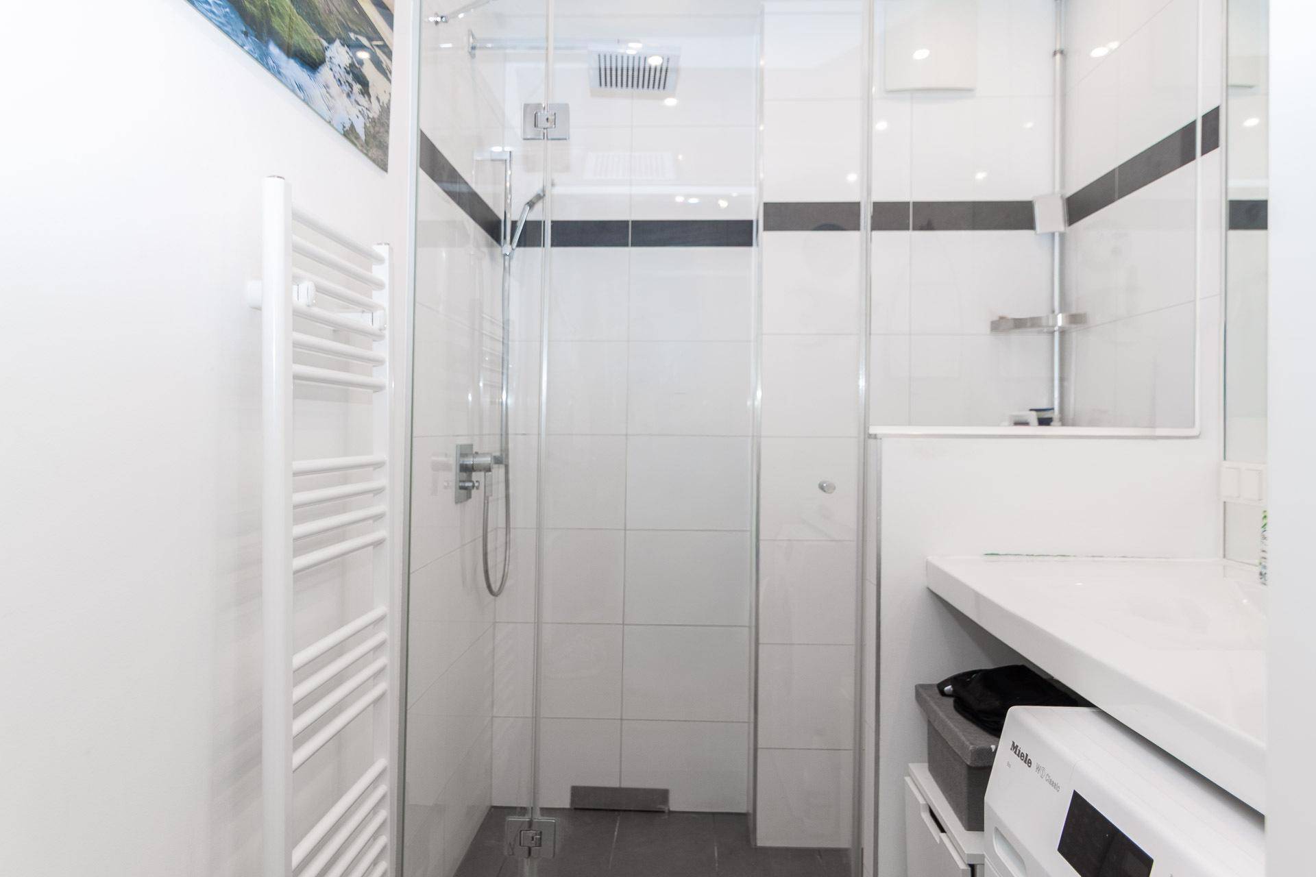 Helles Badezimmer mit begehbarer Dusche, beheiztem Handtuchhalter und modernen Fliesen.