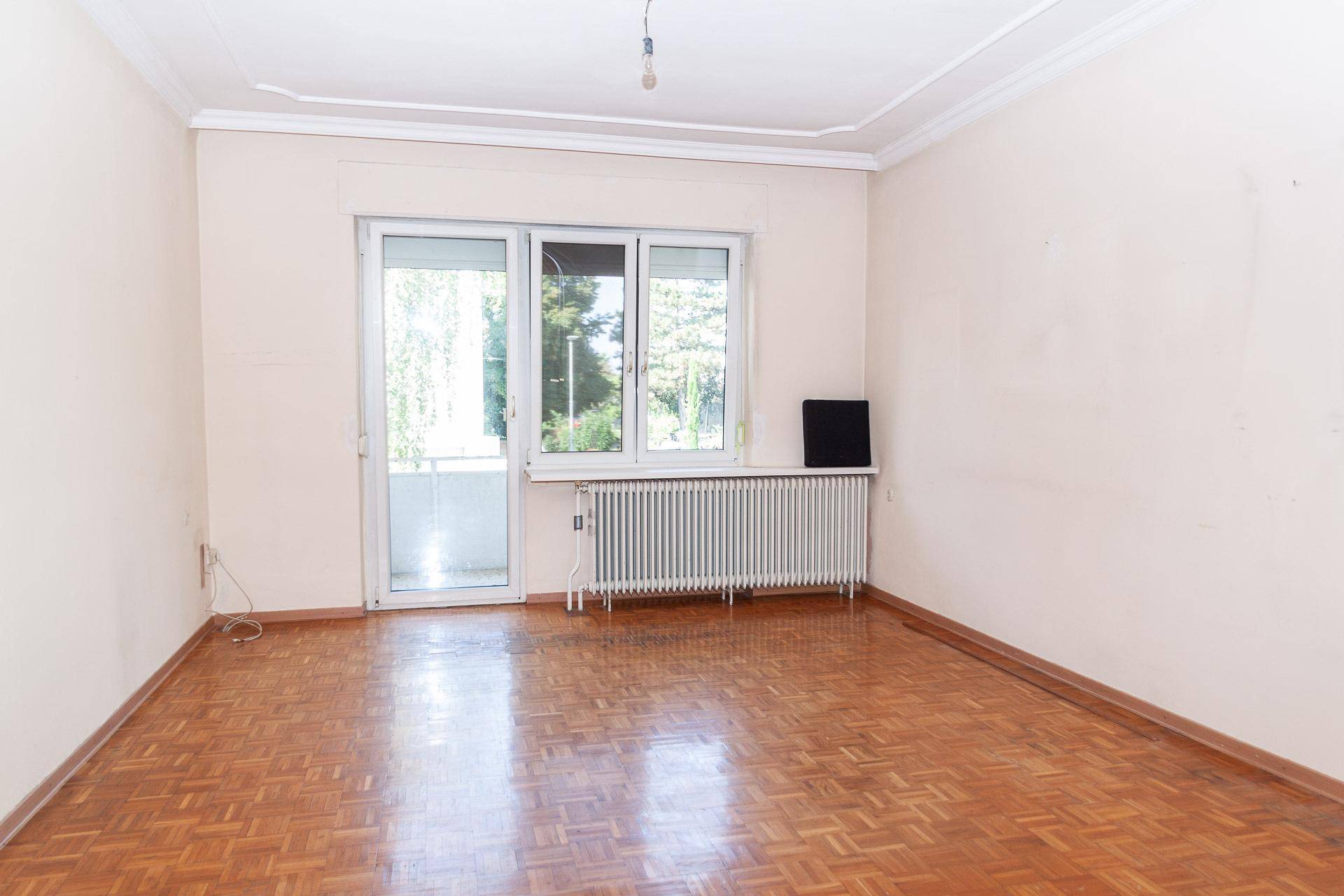 Wohnzimmer mit Parkettboden und Zugang zu einem Balkon, ideal für helle Stunden.