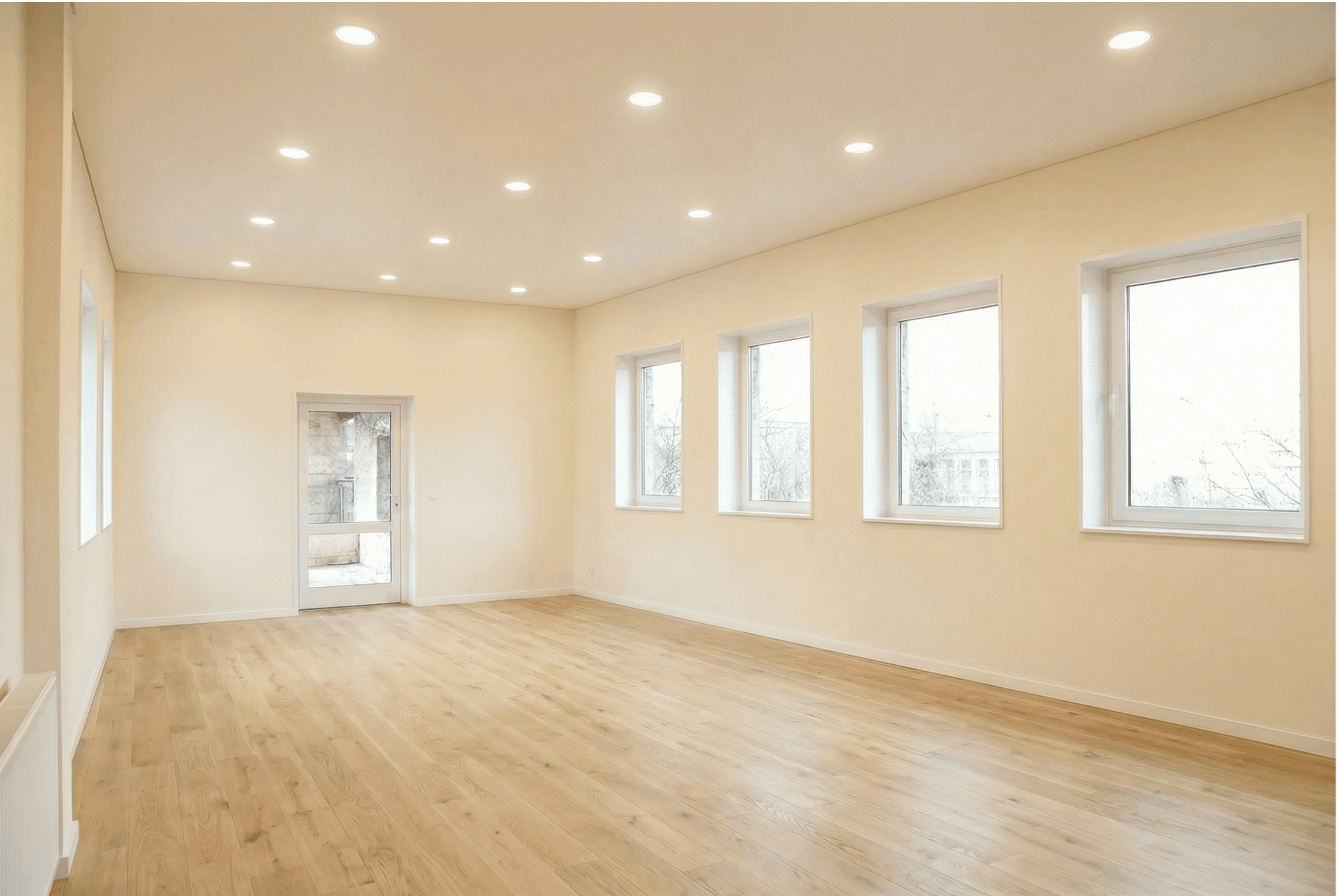 Heller, geräumiger Wohnbereich mit modernem Holzboden, vielen Fenstern und integrierter Deckenbeleuchtung.