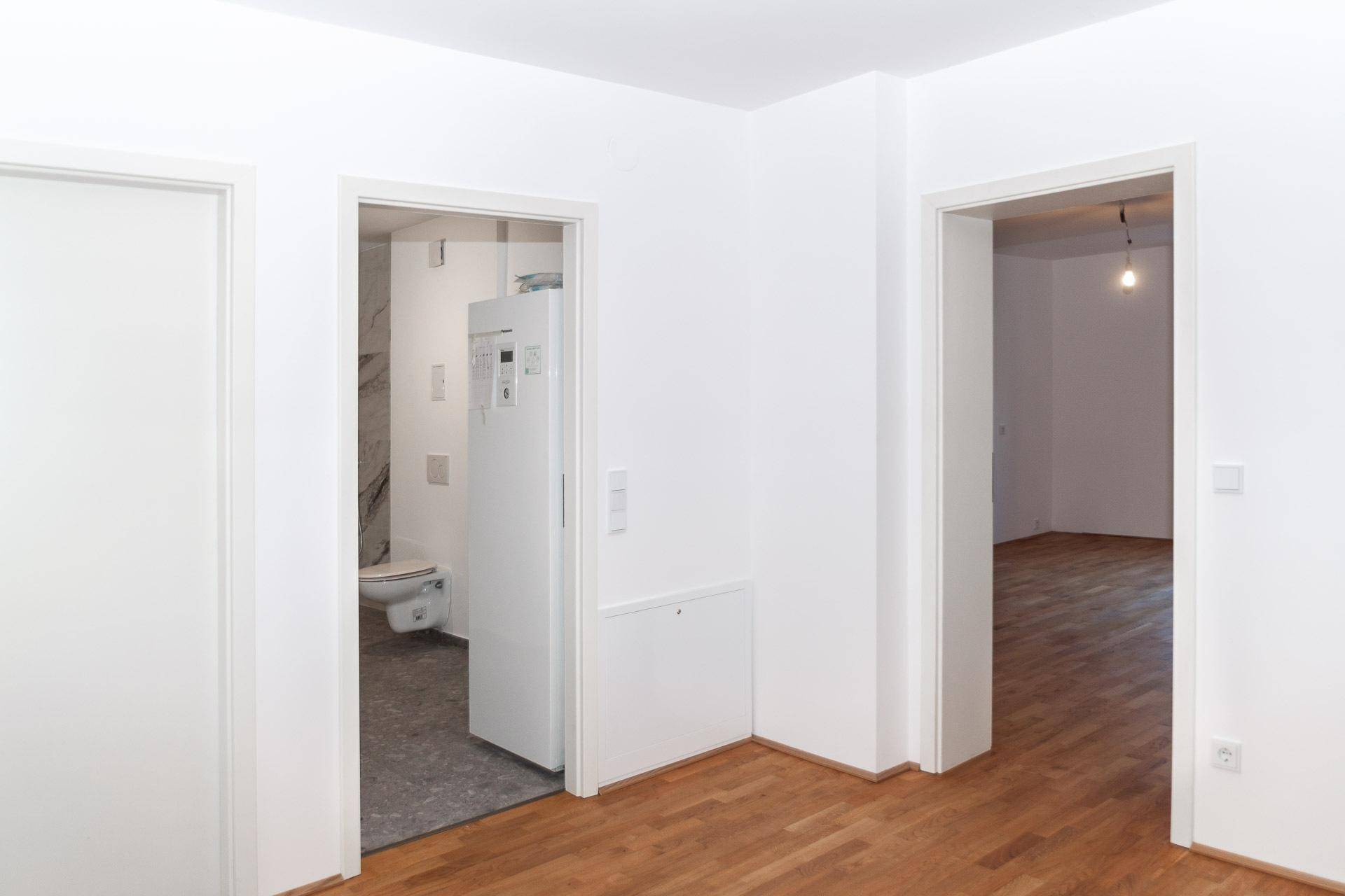 Flur mit Holzboden und Türen zu verschiedenen Räumen, inklusive einem Badezimmer.