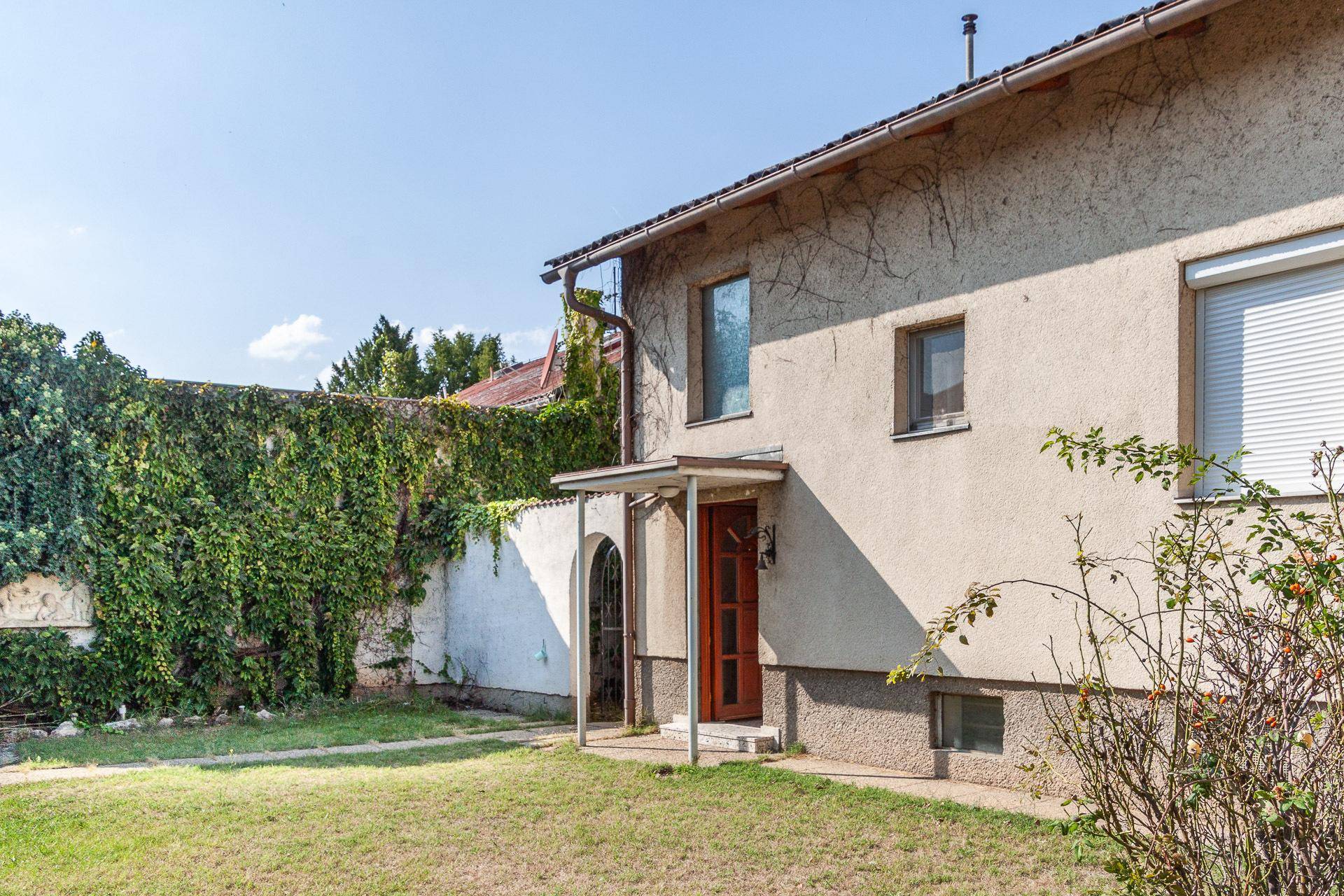 Rückseite des Hauses mit großem Garten, bewachsenen Wänden und einem weiteren Eingang.