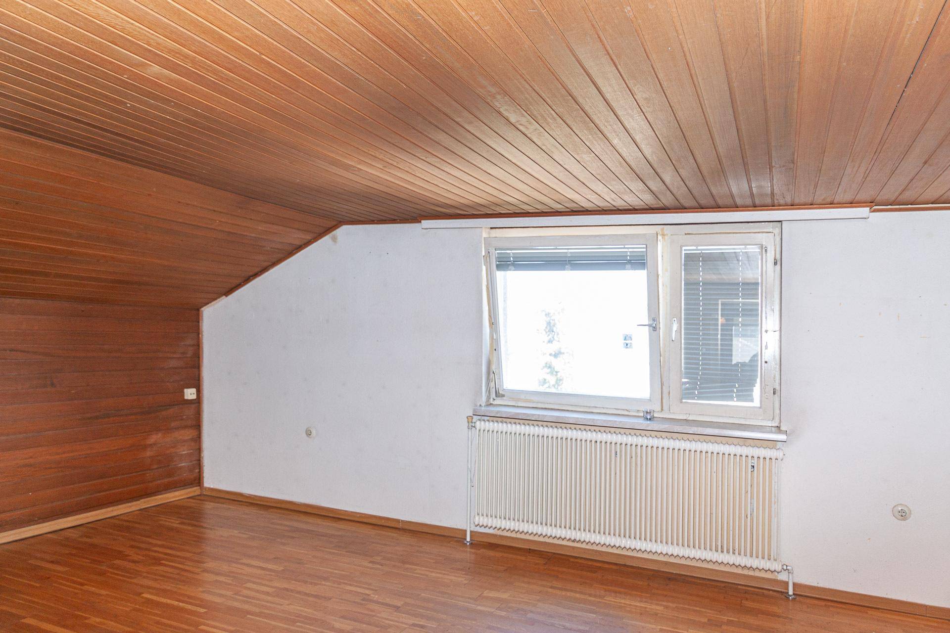 Dachzimmer mit Holzdecke, Parkettboden und Fenster, das viel Potenzial bietet.