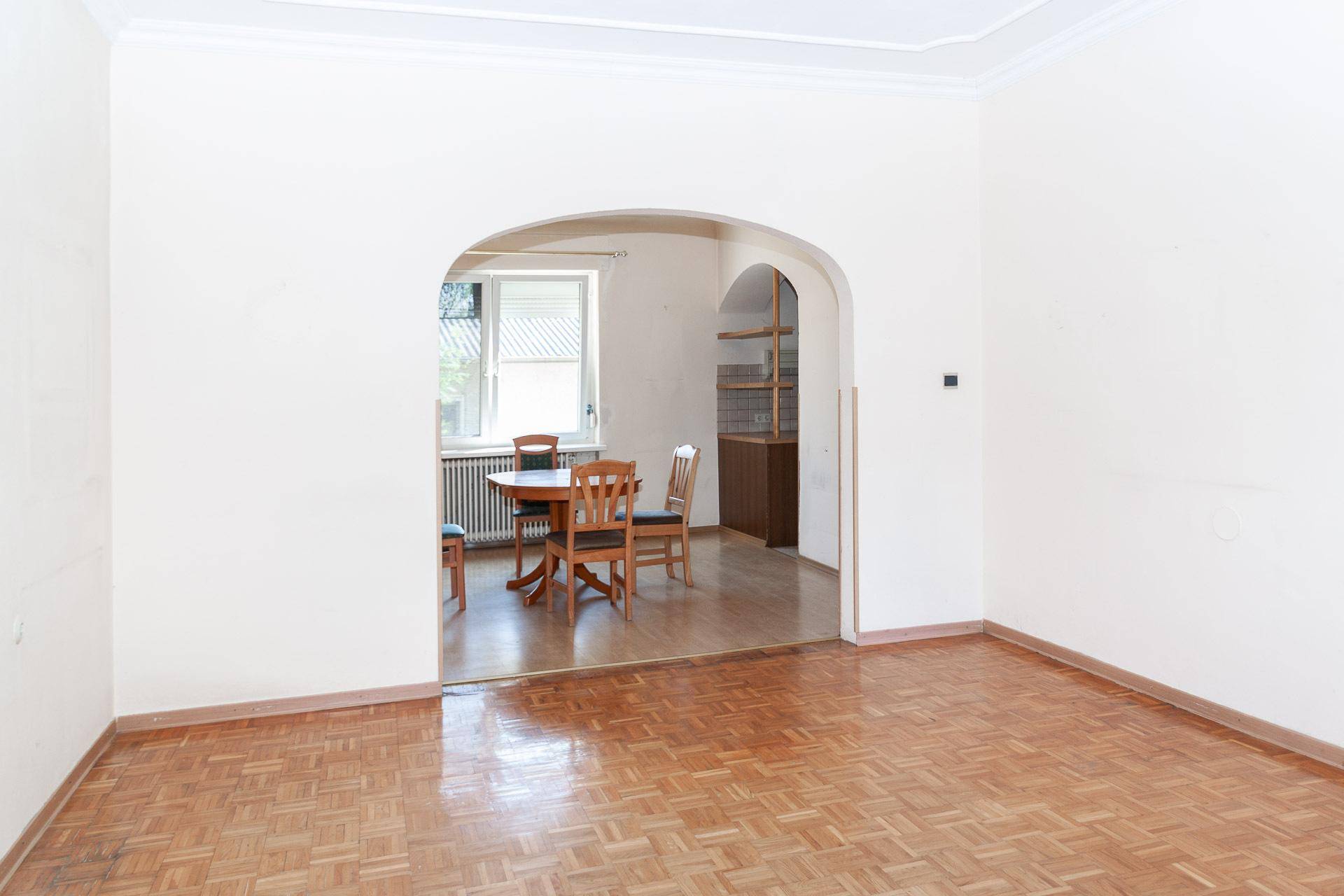 Geräumiges Wohnzimmer mit Parkettboden und einem Bogen, der zum Essbereich führt.