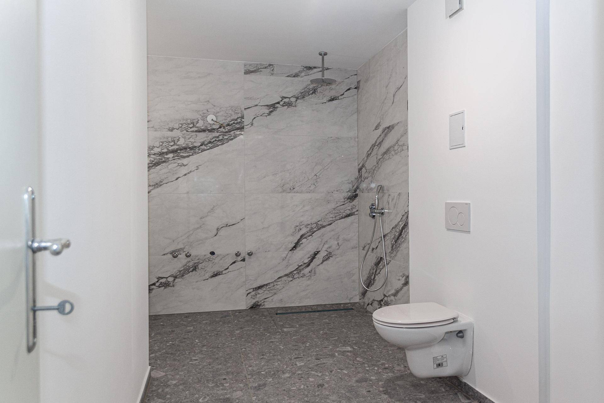 Modernes Badezimmer mit großformatigen Marmorfliesen, bodengleicher Dusche und Wand-WC.