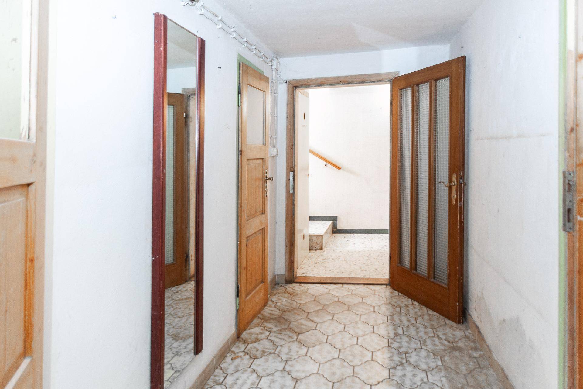 Kellerflur mit gefliestem Boden und Holztüren, der zu verschiedenen Kellerräumen führt.