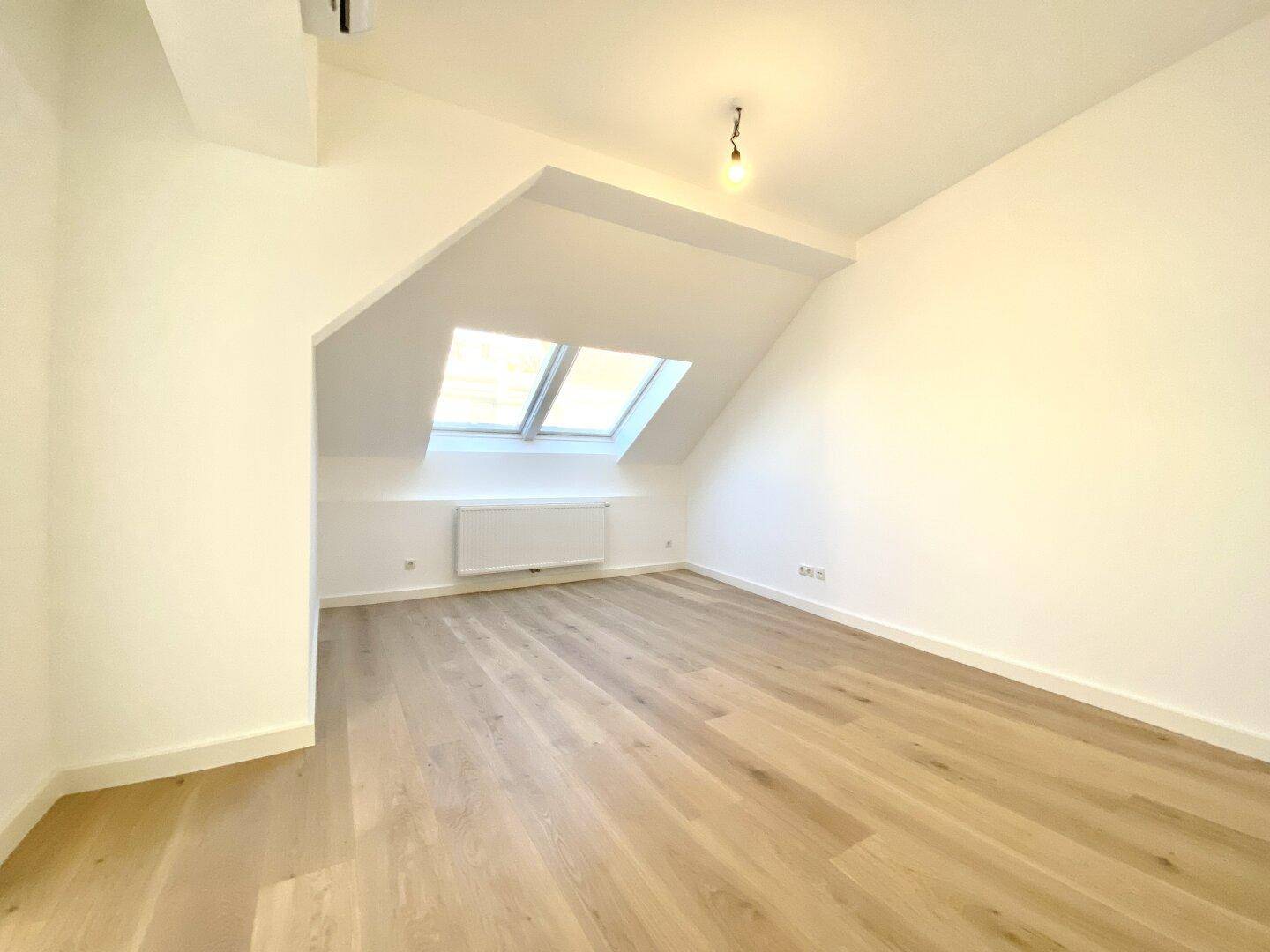 Heller, leerer Raum mit Holzboden, Dachschräge und großem Dachfenster, vielseitig nutzbar.