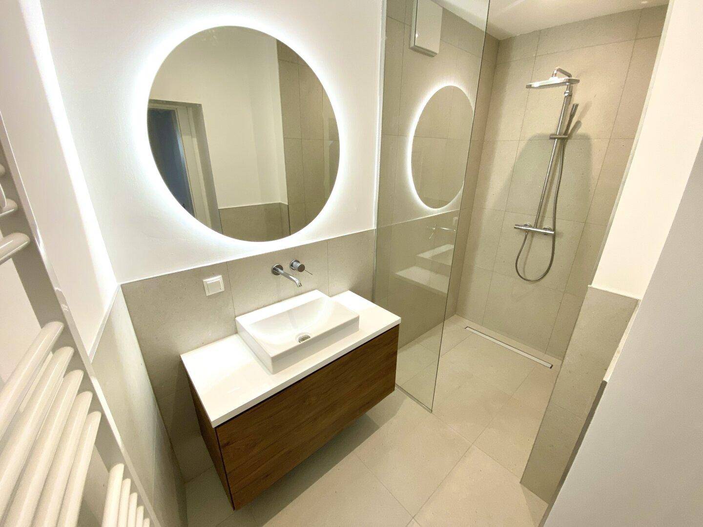 Modernes Badezimmer mit begehbarer Dusche, Einzelwaschbecken und beleuchtetem Spiegel.