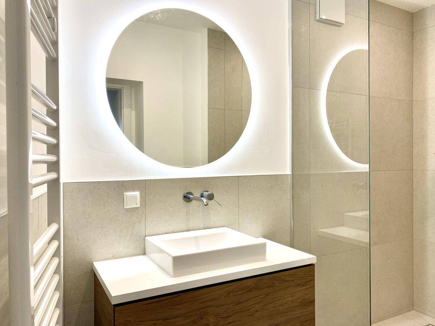 Einzelwaschbecken mit modernem Wasserhahn und großem, beleuchtetem Spiegel im Badezimmer.