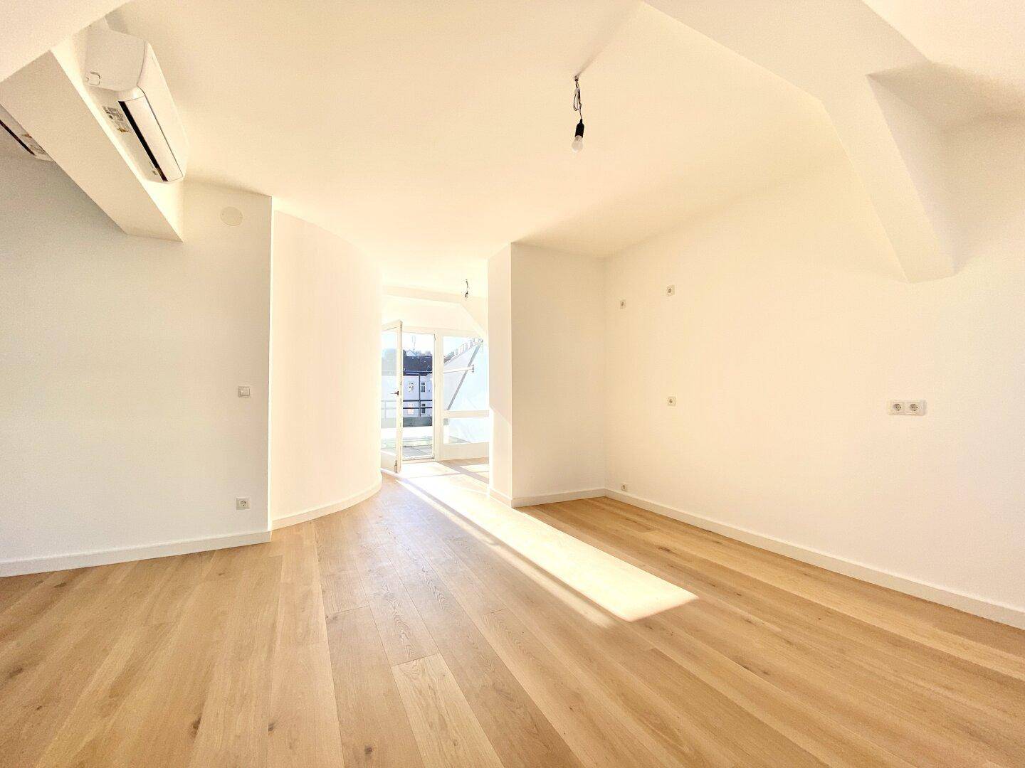 Leerer Raum mit Holzboden, Klimaanlage und Zugang zu einem Außenbereich, ideal für individuelle Gestaltung.