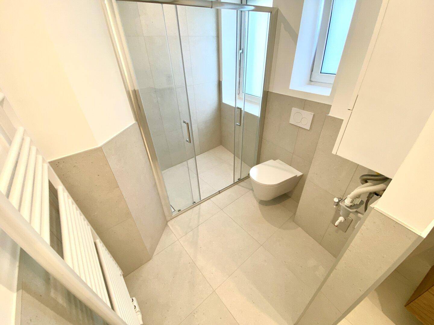 Modernes Badezimmer mit begehbarer Dusche, Wand-WC und Fenster für natürliche Belüftung.