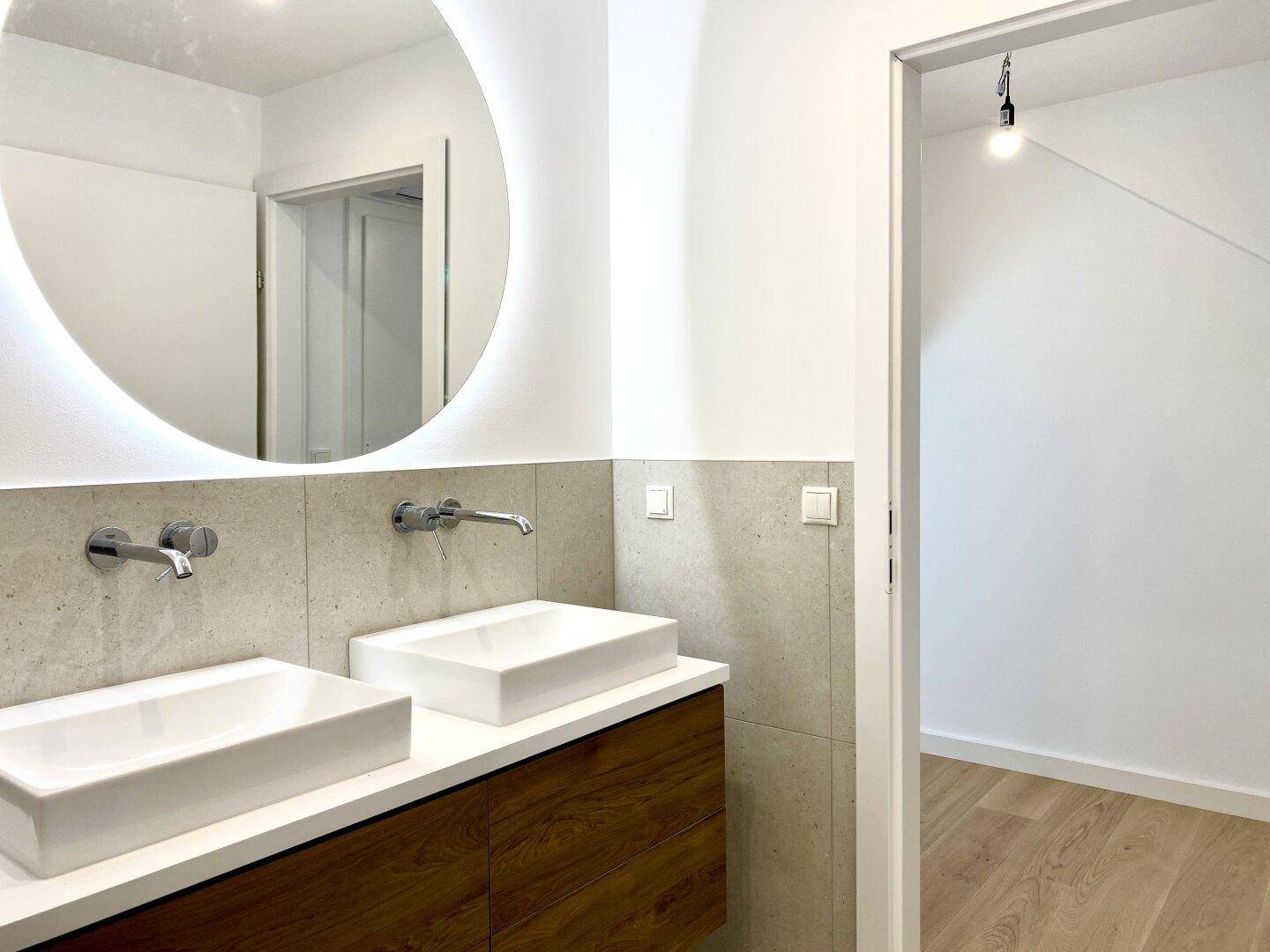Doppelwaschbecken mit modernen Armaturen und großem, beleuchtetem Spiegel im Hauptbadezimmer.