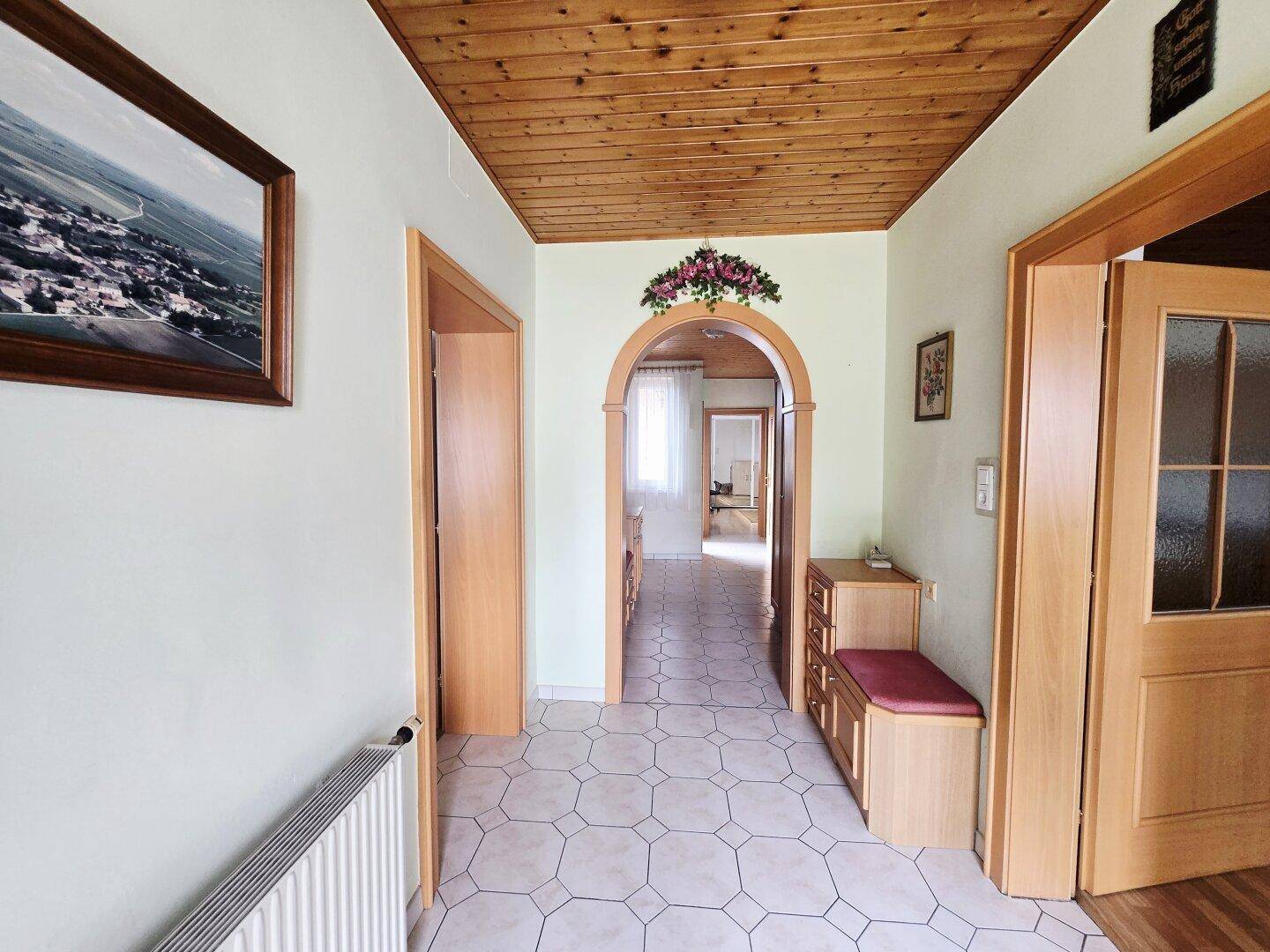 Heller Flur mit Holzdecke, Fliesenboden und einem Bogen zu weiteren Räumen.