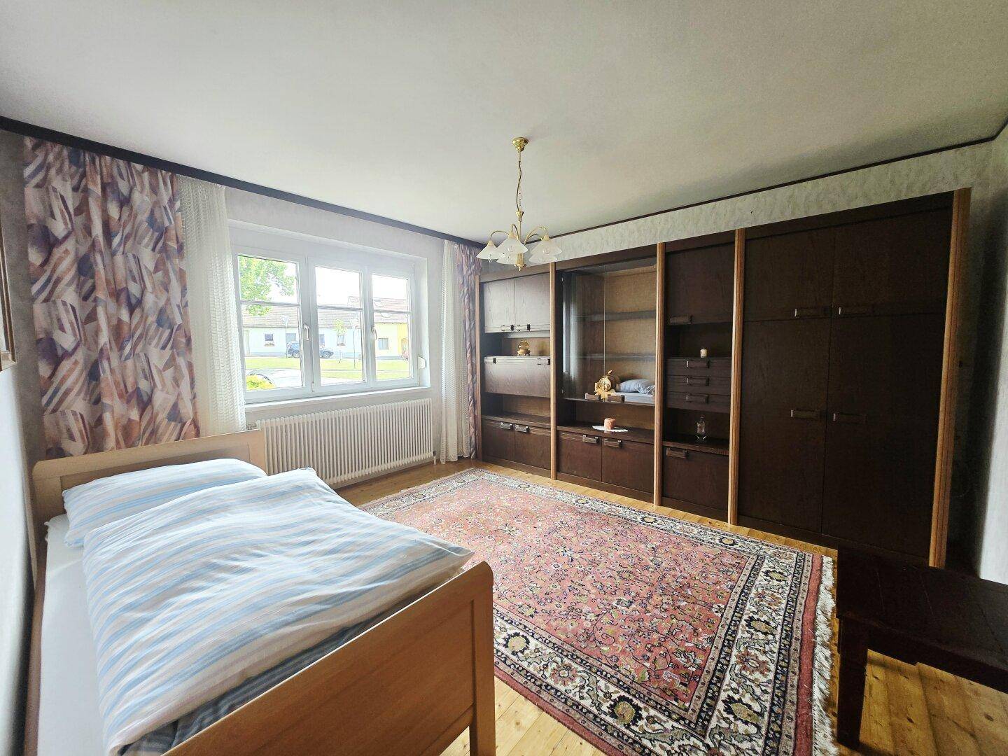 Schlafzimmer mit Holzboden, großem Fenster und einem Einbauschrank an der Wand.