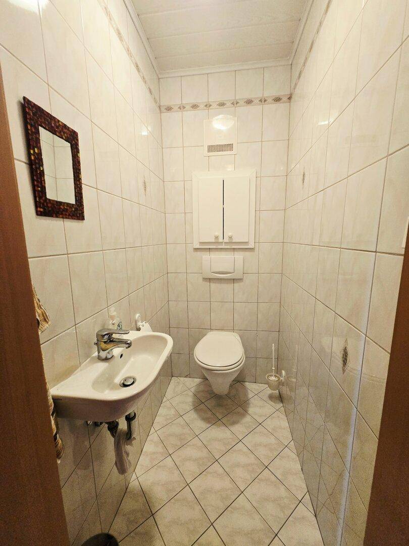 Kleines Gäste-WC mit weißen Fliesen, wandhängendem WC und einem Waschbecken.