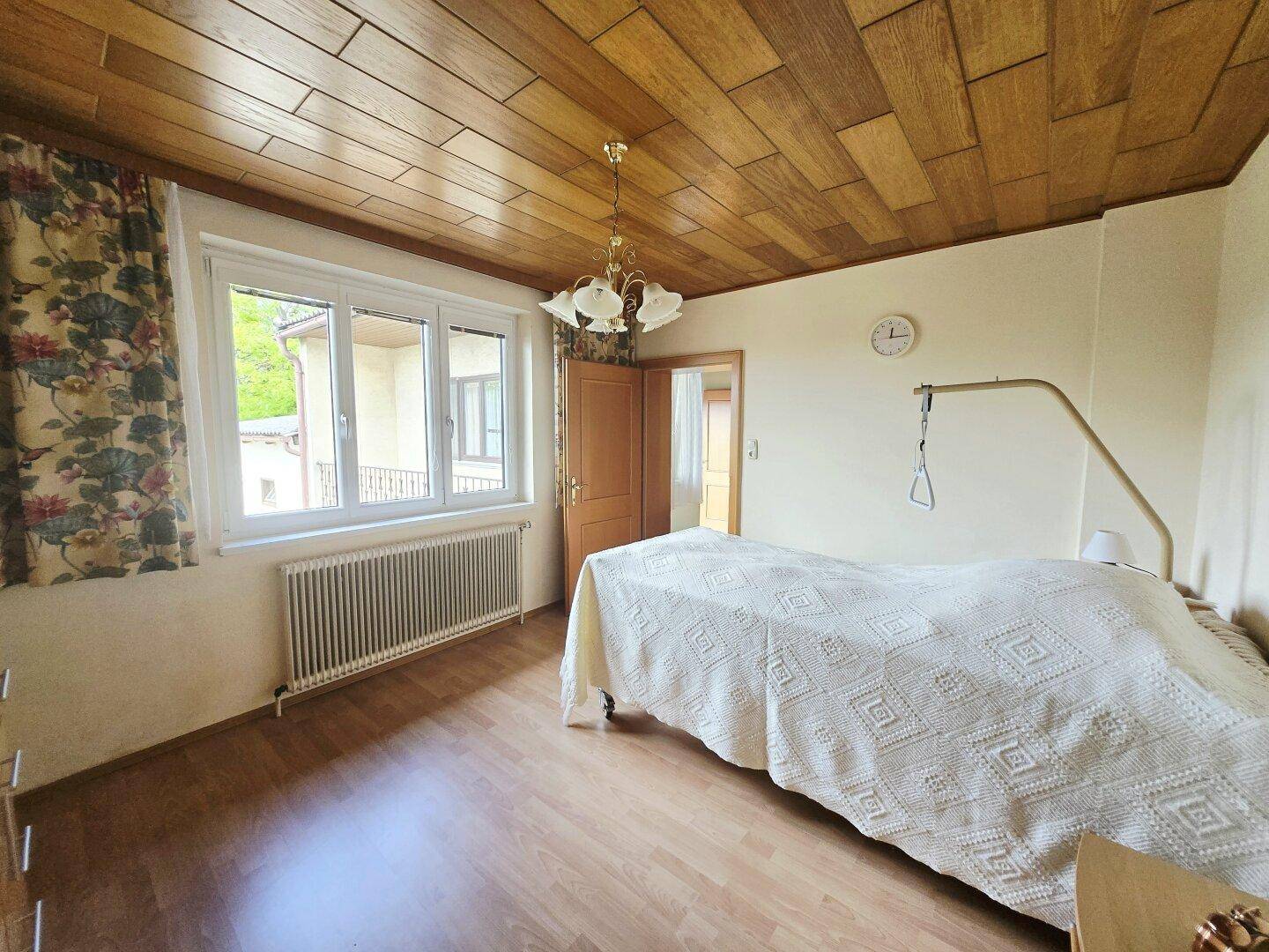 Schlafzimmer mit Holzdecke, Laminatboden und einem Fenster mit Blick nach draußen.