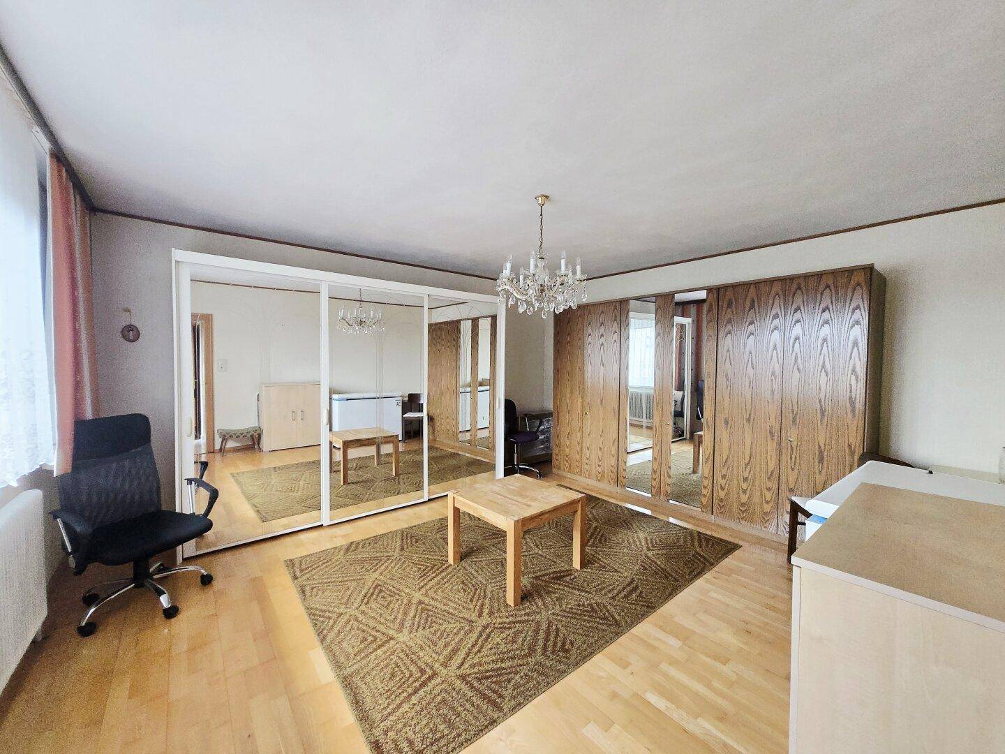 Geräumiges Schlafzimmer mit Laminatboden, Spiegelschränken und einem Kronleuchter.